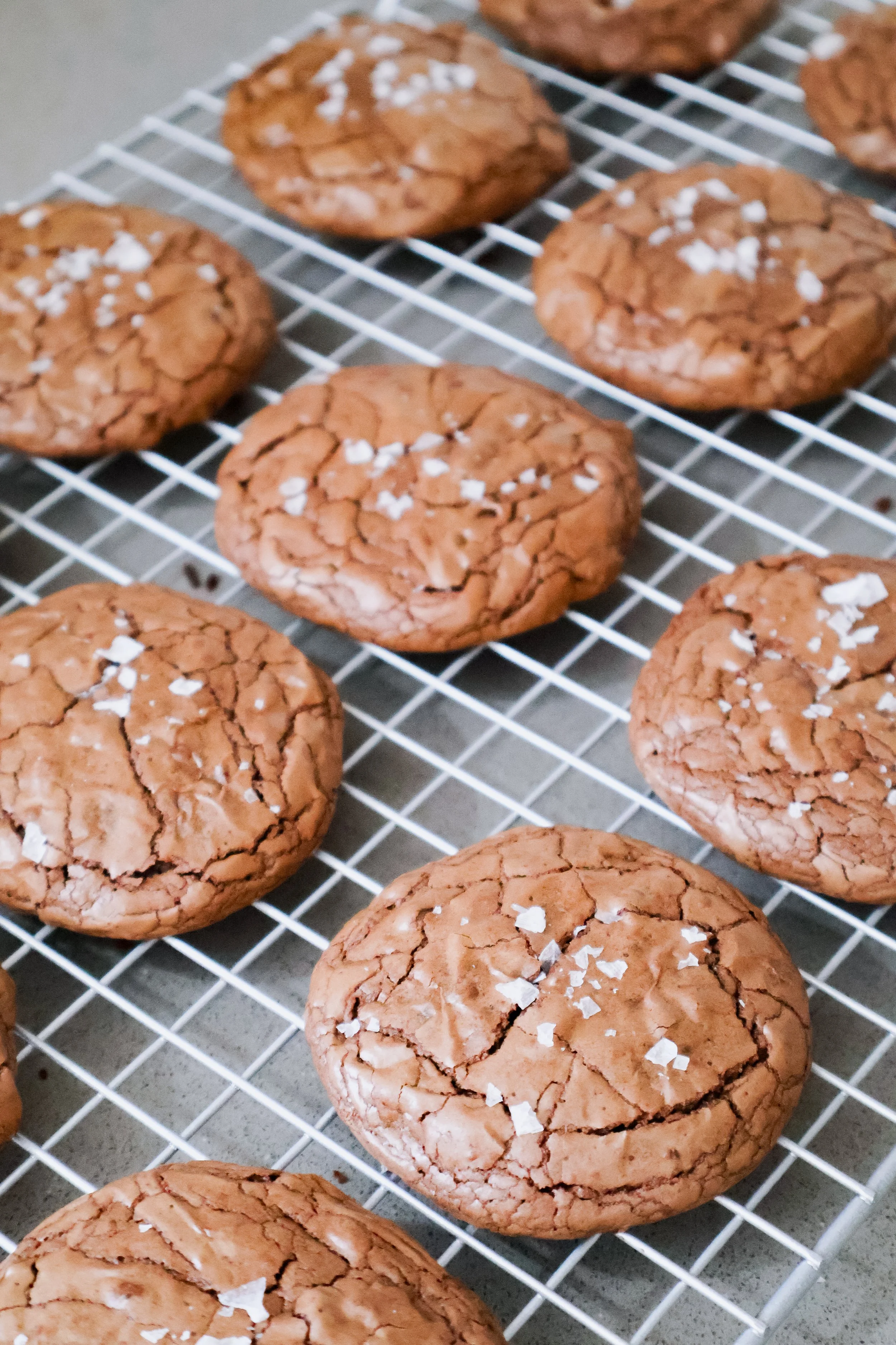 A wire cooling rack with freshly baked chocolate cookies sprinkled with sea salt.