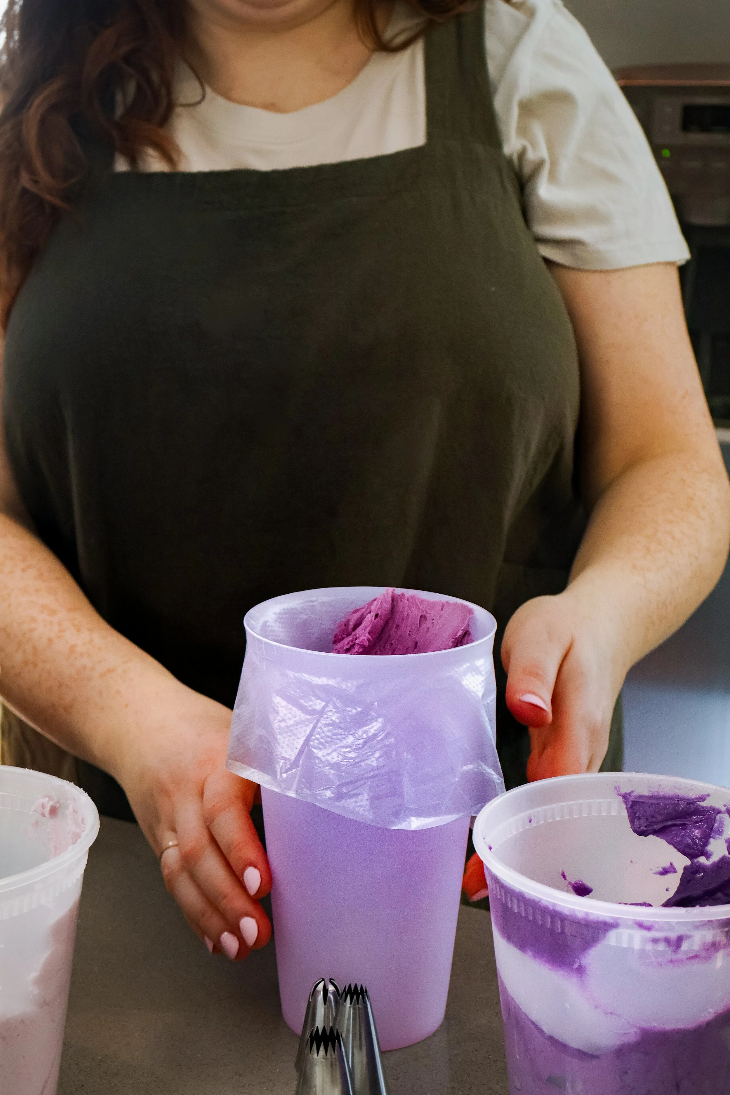 Person holding a lavender cup with purple ice cream inside, with other similar cups on the table.