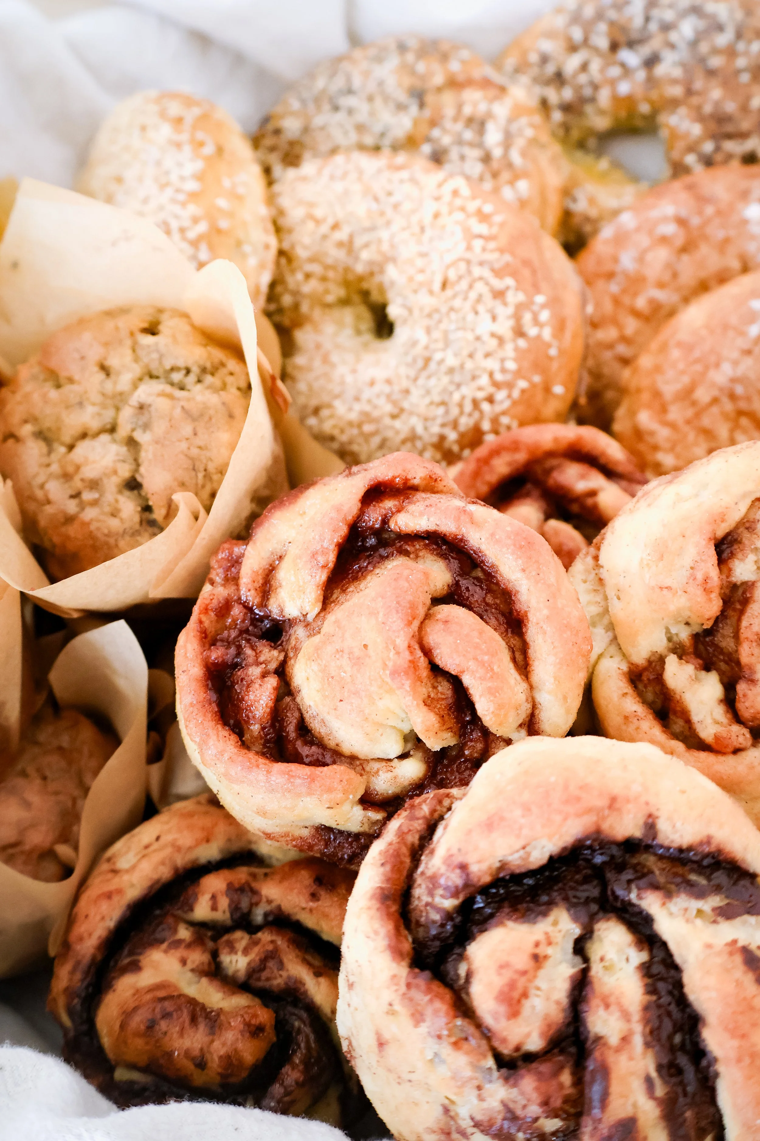 Assorted baked goods including cinnamon rolls with chocolate filling, muffins, and bagels