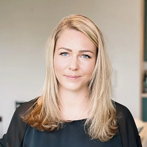 A portrait of a young woman with blonde hair and blue eyes, wearing a black top, smiling softly at the camera.