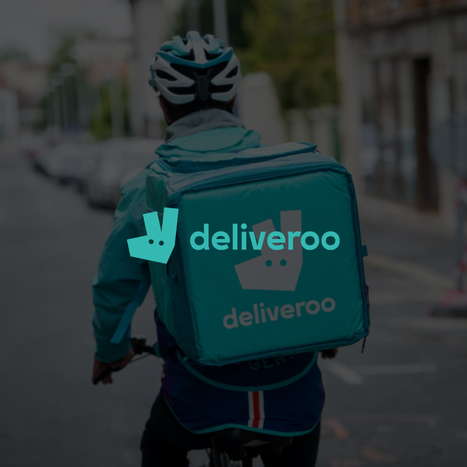 Delivery person riding a bicycle with a large teal delivery bag labeled 'Deliveroo' on a city street.