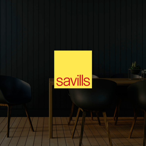 A sign with the Savills logo placed in a modern black and wood interior space with chairs and a side table.