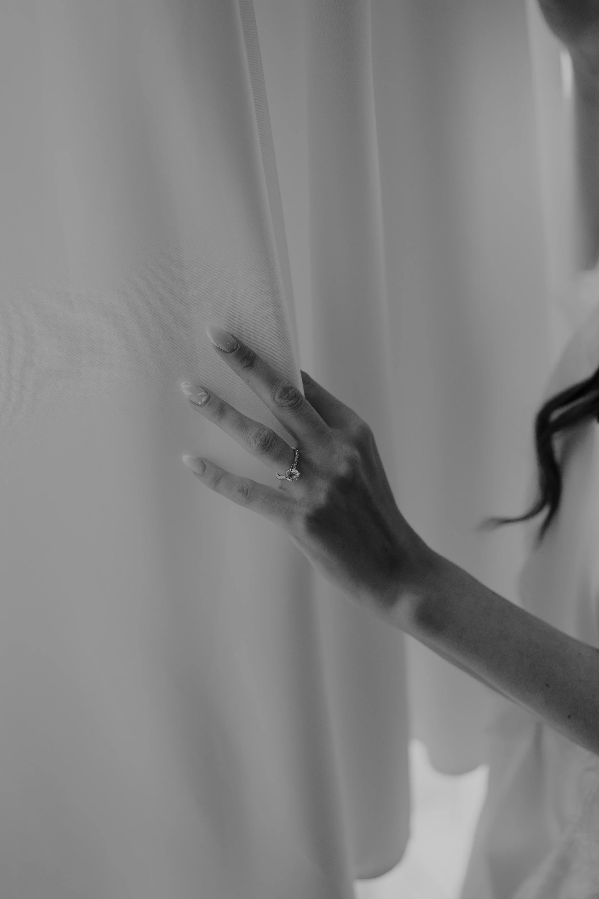 Close-up of a person's hand with a ring, touching a curtain.
