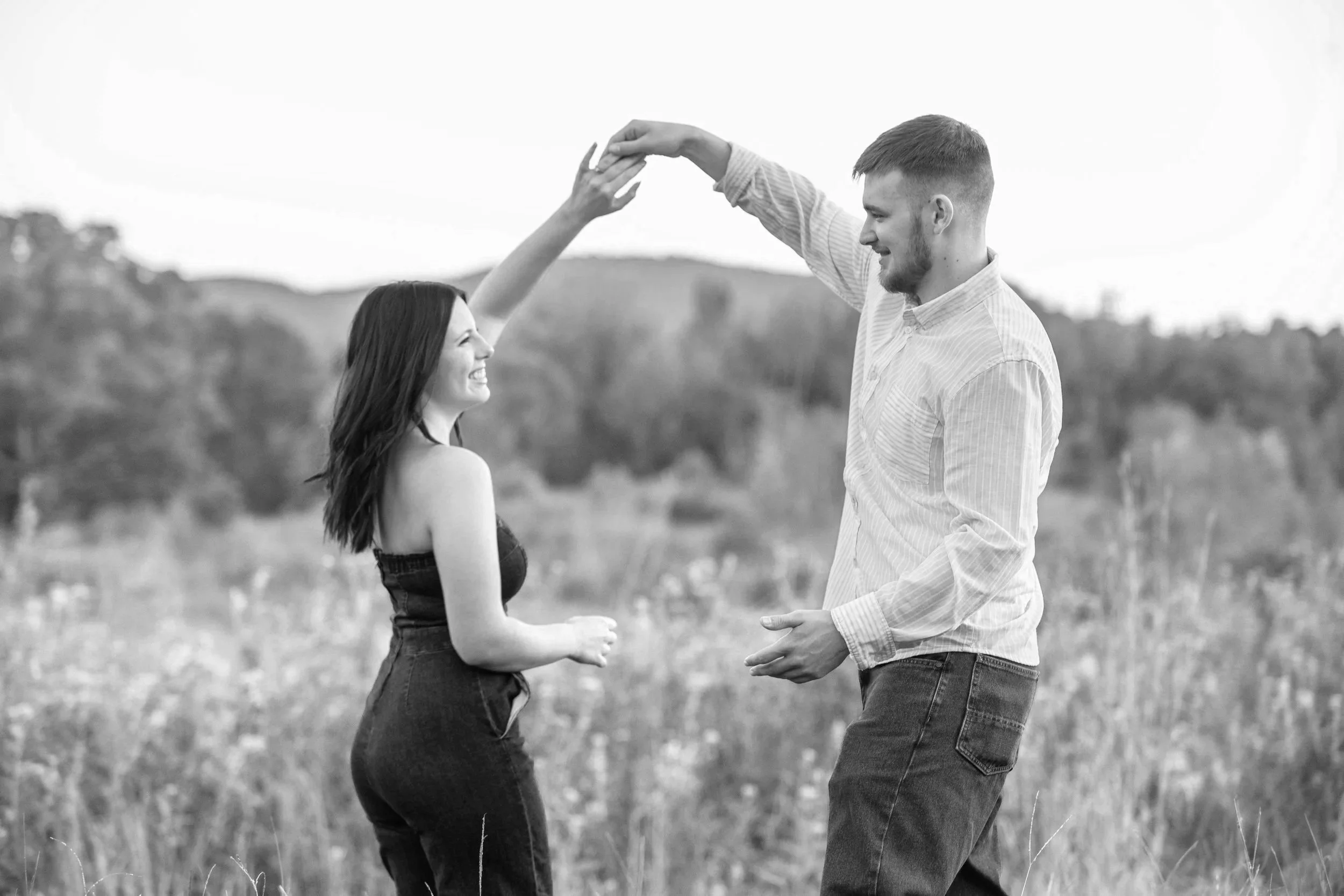 A young man and woman dancing outdoors in a field, smiling and holding hands.