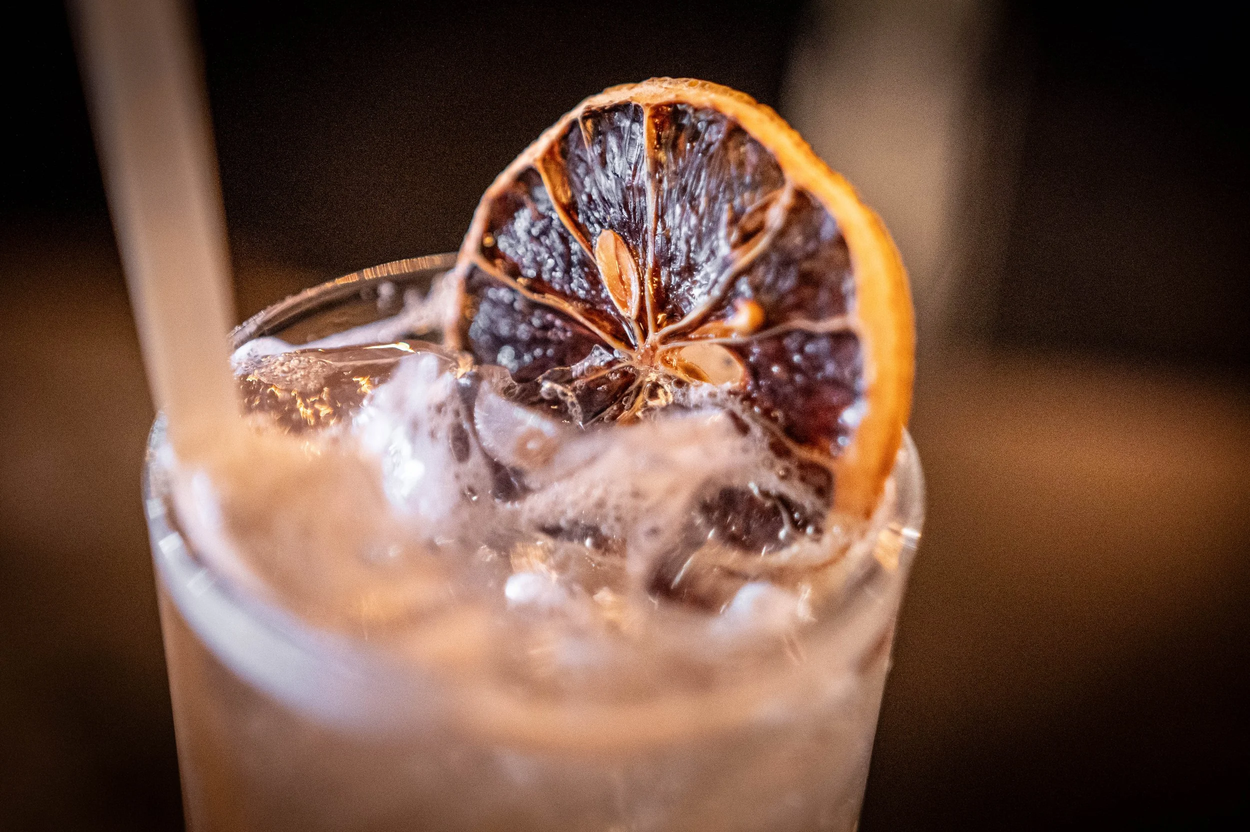A dried orange rests on top of a cocktail drink.