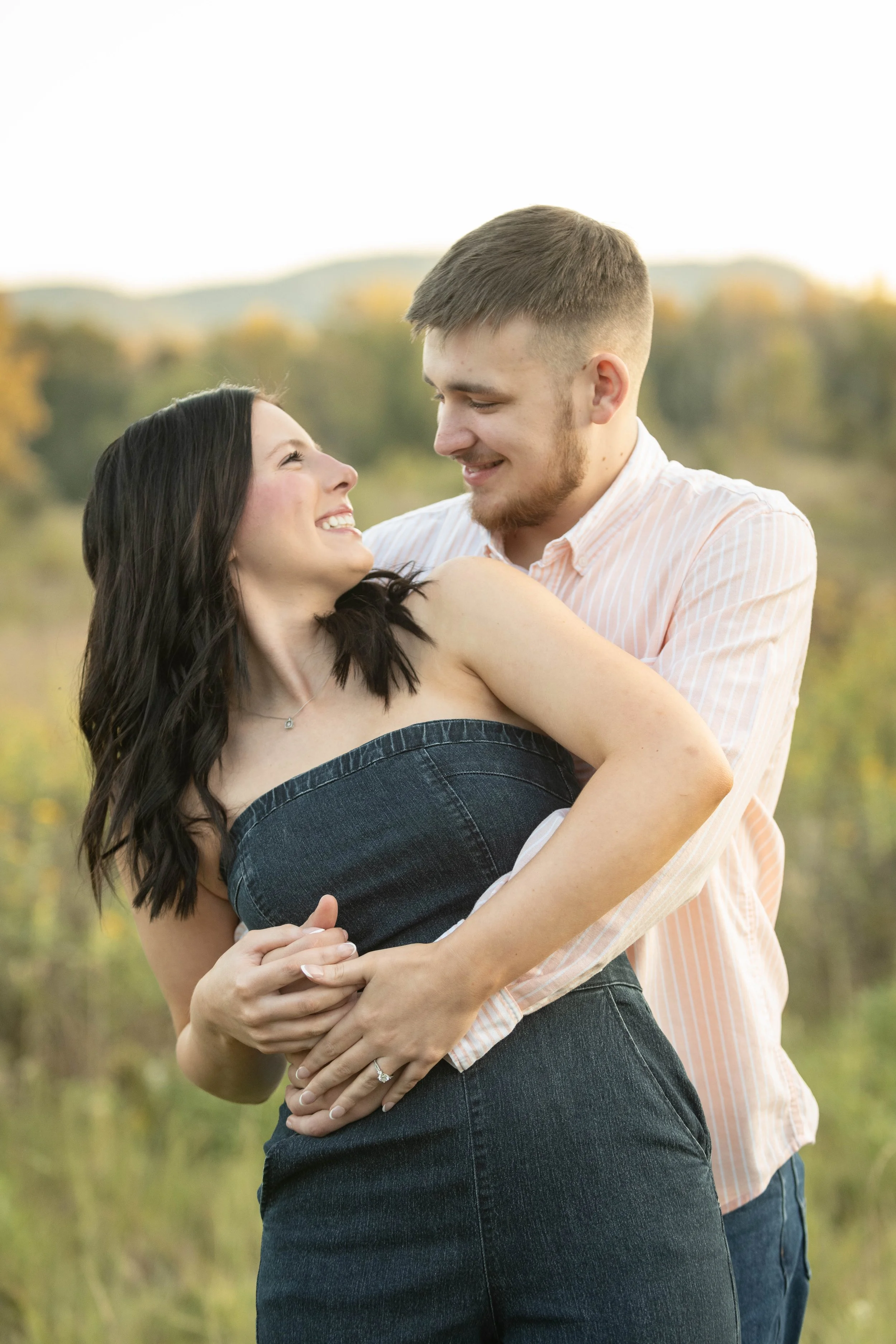 A happy couple embracing outdoors with mountains and trees in the background.