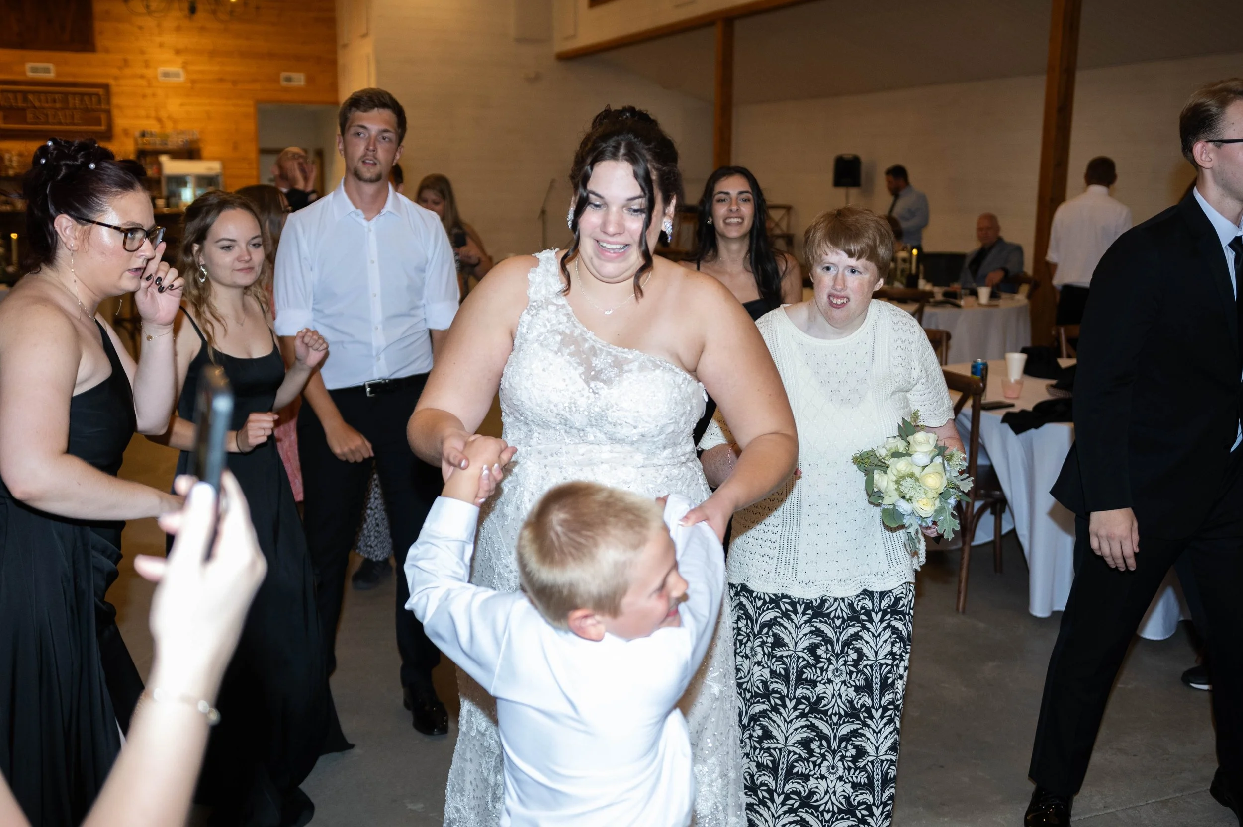Bride dancing with a young boy at a wedding reception surrounded by guests.