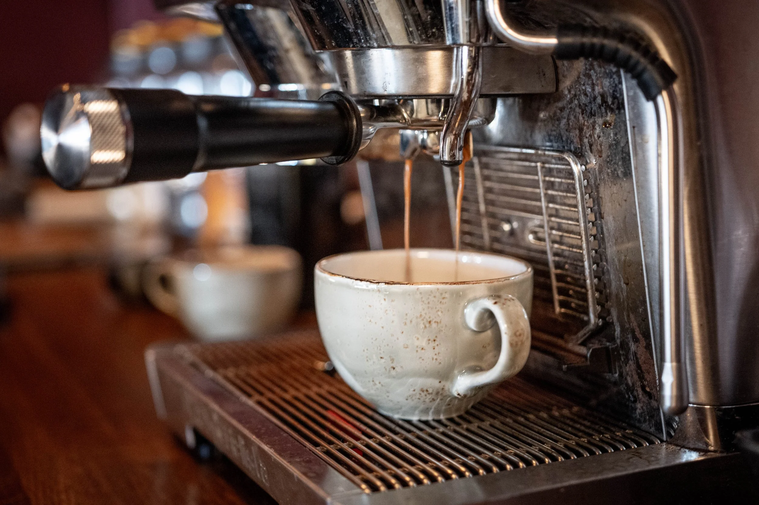 A coffee machine brewing espresso into a vintage white ceramic mug with a handle on a metal drip tray.