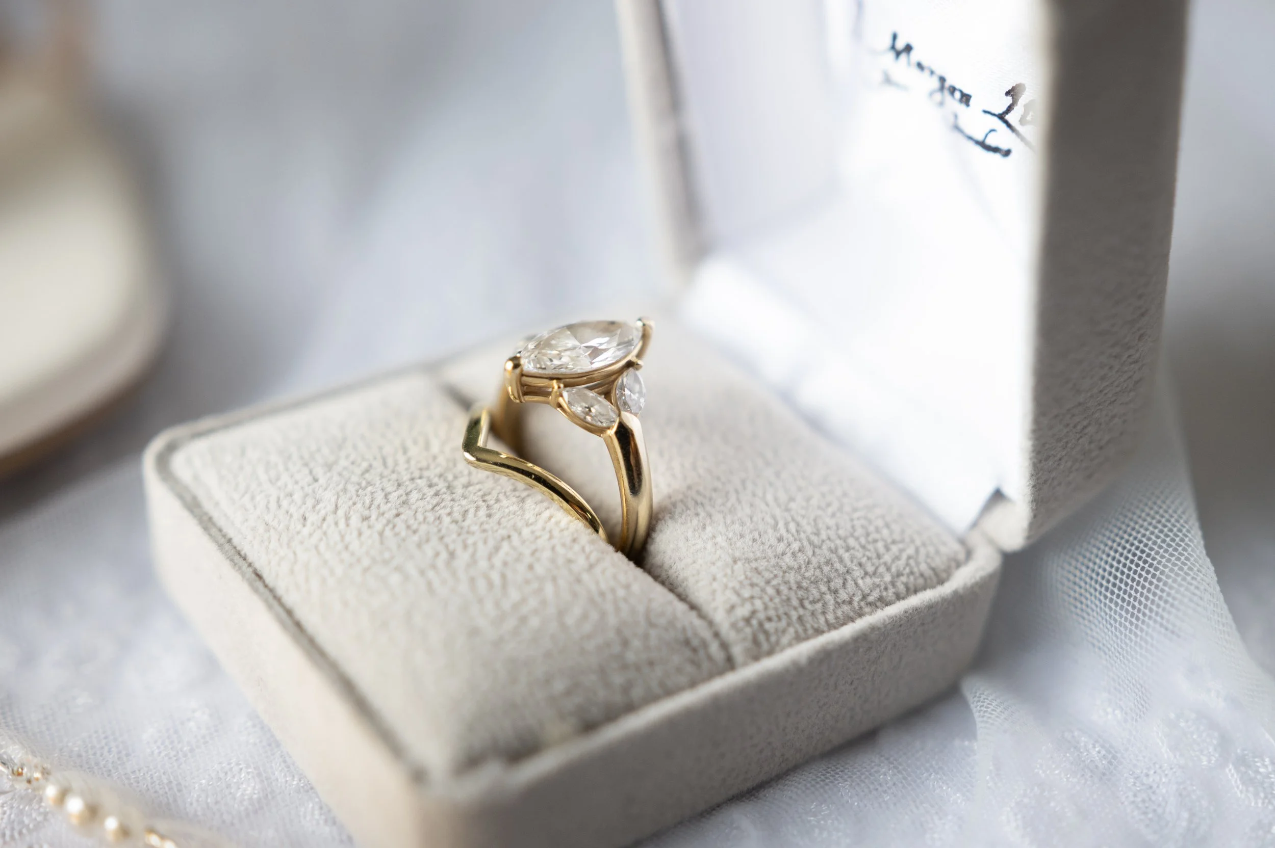 A gold ring with a large clear gemstone and smaller gemstones on a white cushioned jewelry box.