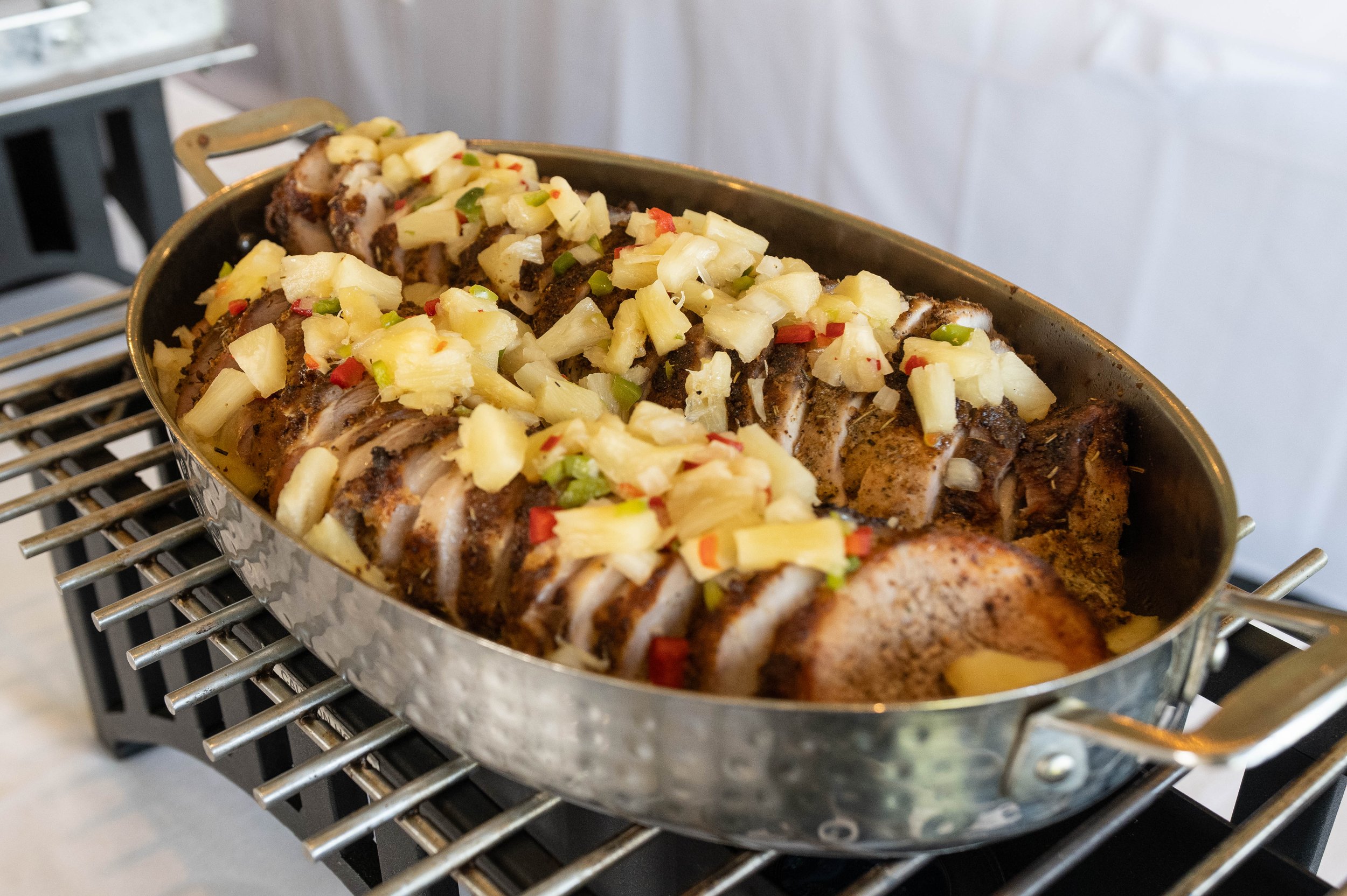 A large roasted pork loin topped with chopped pineapple and red and green peppers in a metal roasting pan