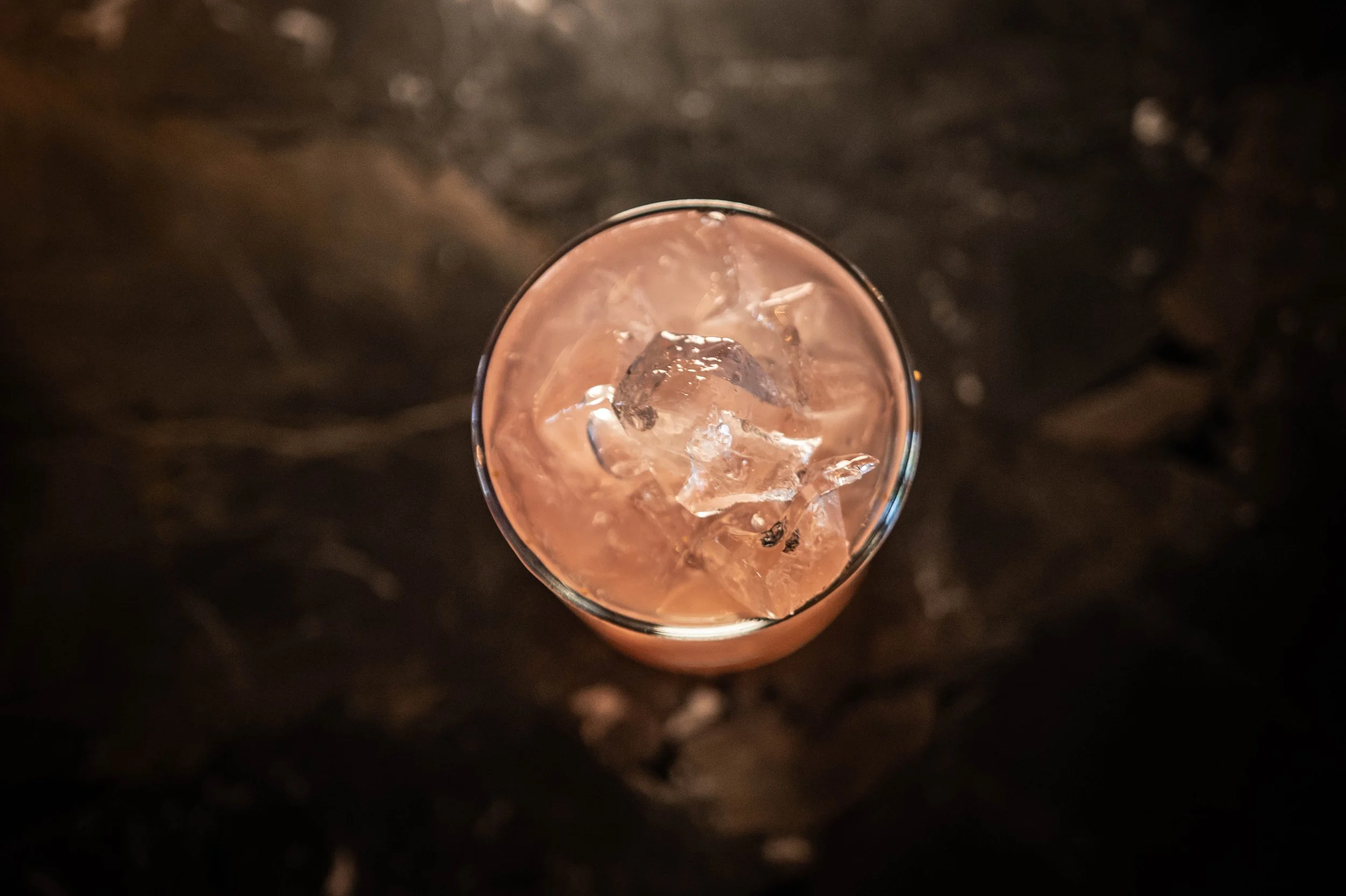 Top-down view of a glass filled with a pink beverage and ice cubes, placed on a dark surface.