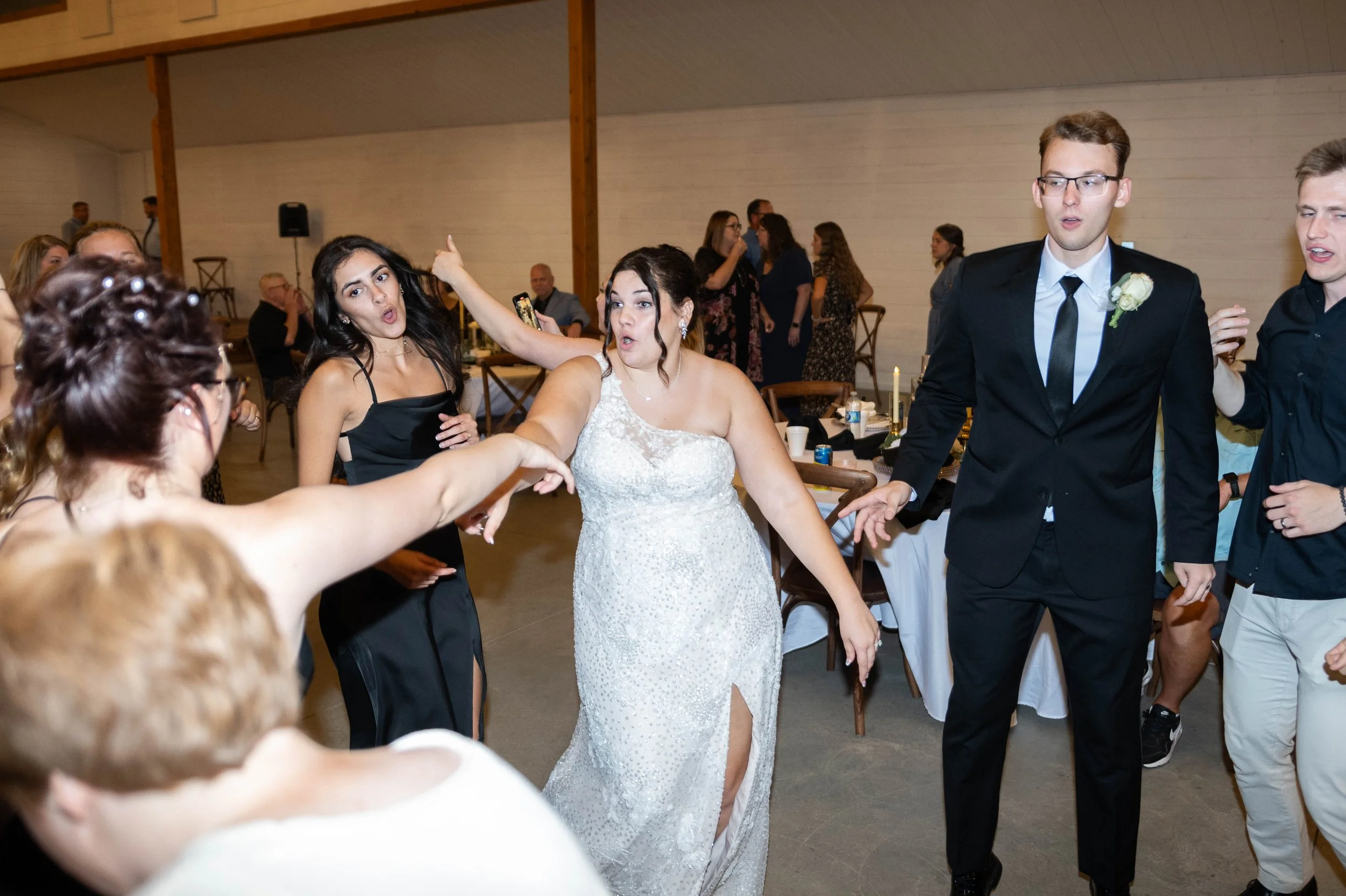 People dancing and celebrating at a wedding reception, with a bride in a white dress and a groom in a black suit.