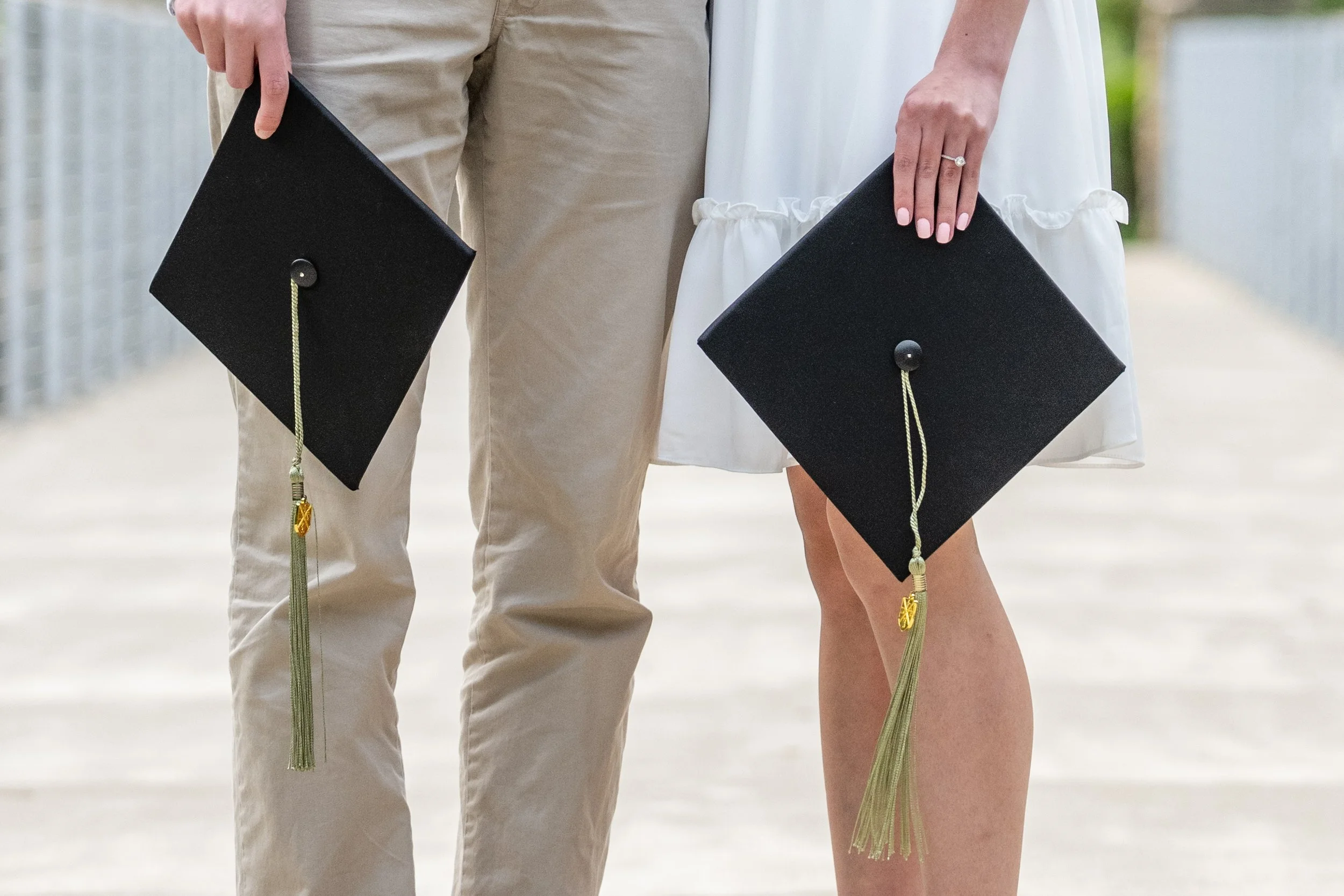A man and woman in formal attire holding graduation caps in an outdoor setting.
