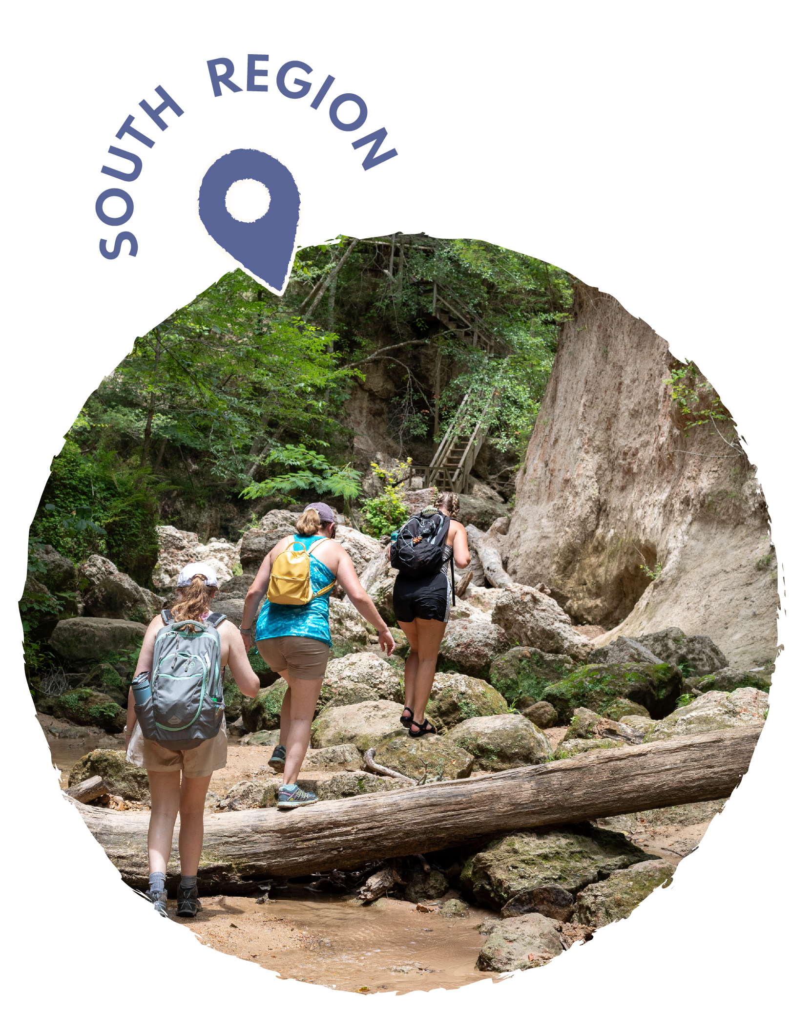 Three women hiking over rocks in a forested area with trees and a wooden staircase in the background.