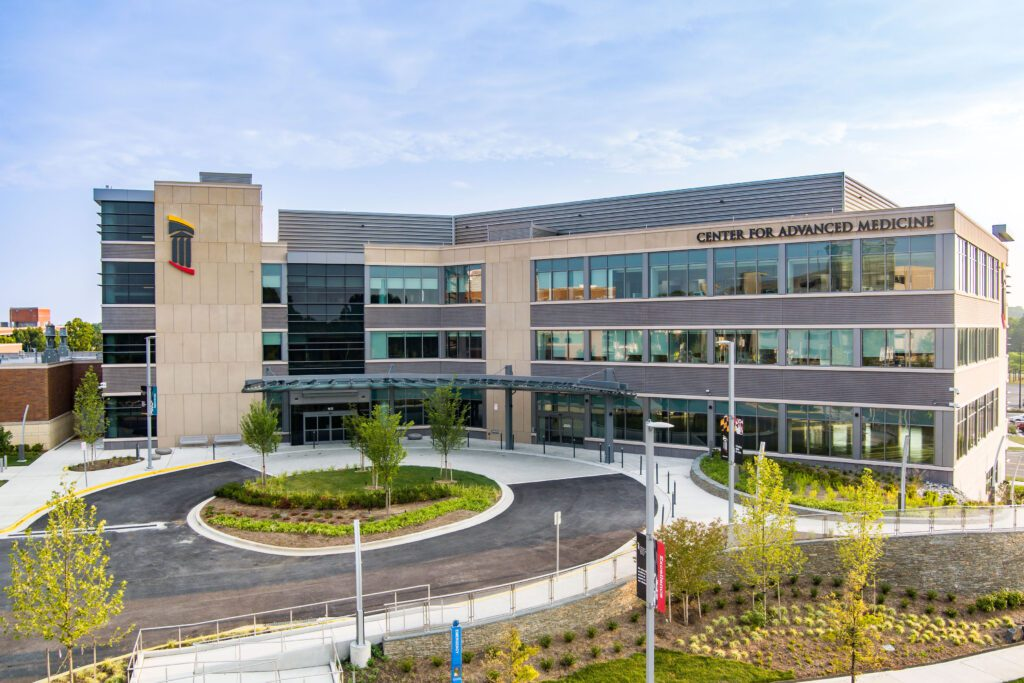 Exterior of a modern medical center building with large glass windows and a sign reading 'Center for Advanced Medicine'.