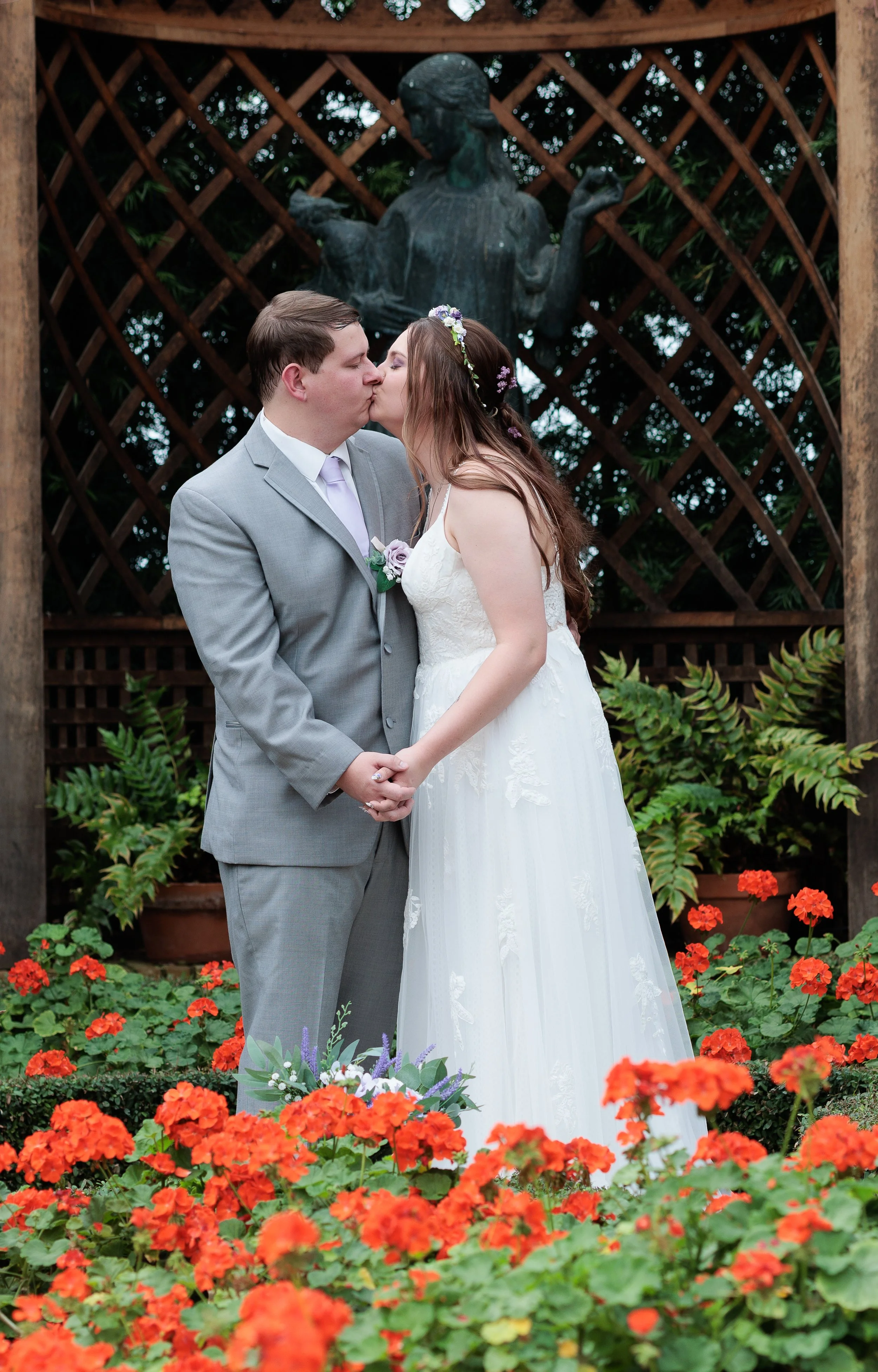 A newlywed couple shares a first kiss while holding hands in a garden surrounded by orange flowers with a wooden trellis at Phipps in Pittsburgh