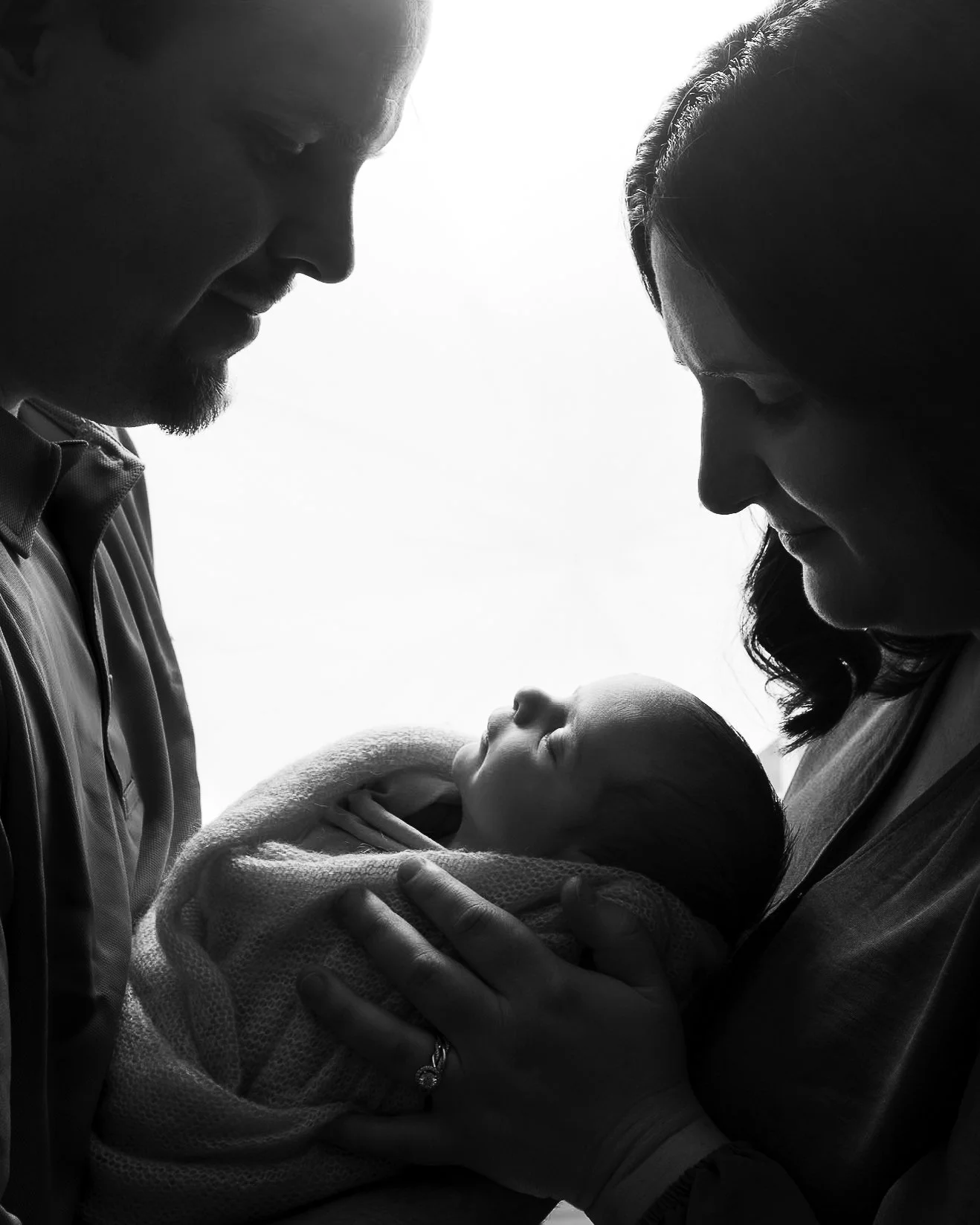Silhouette of a couple holding their newborn baby, facing each other gently, in black and white newborn photography Mcmurray PA