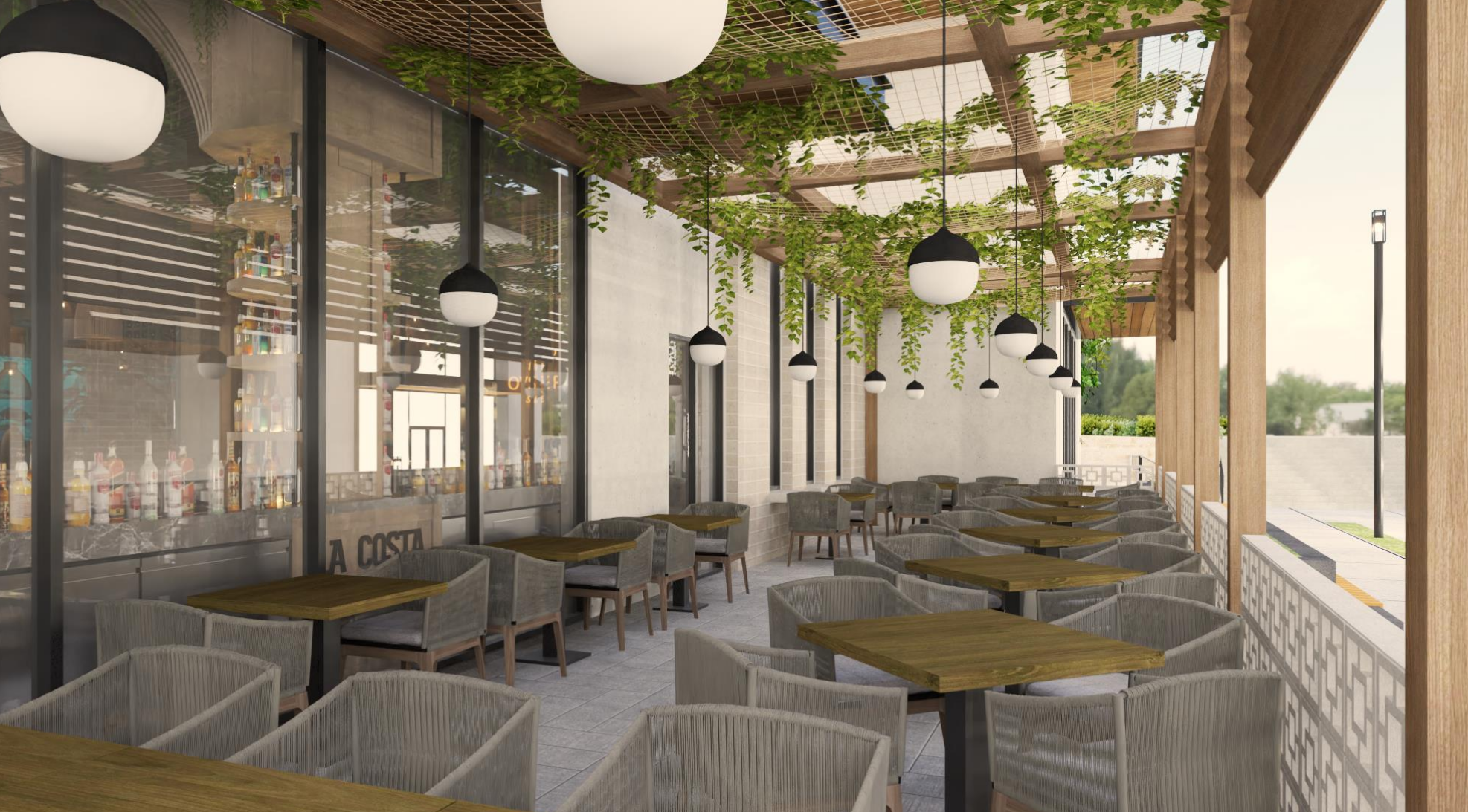 Outdoor patio of a restaurant or cafe with wooden tables, grey upholstered chairs, hanging black and white spherical pendant lights, and green plants hanging from a wooden pergola, with a view of trees and a sidewalk outside.