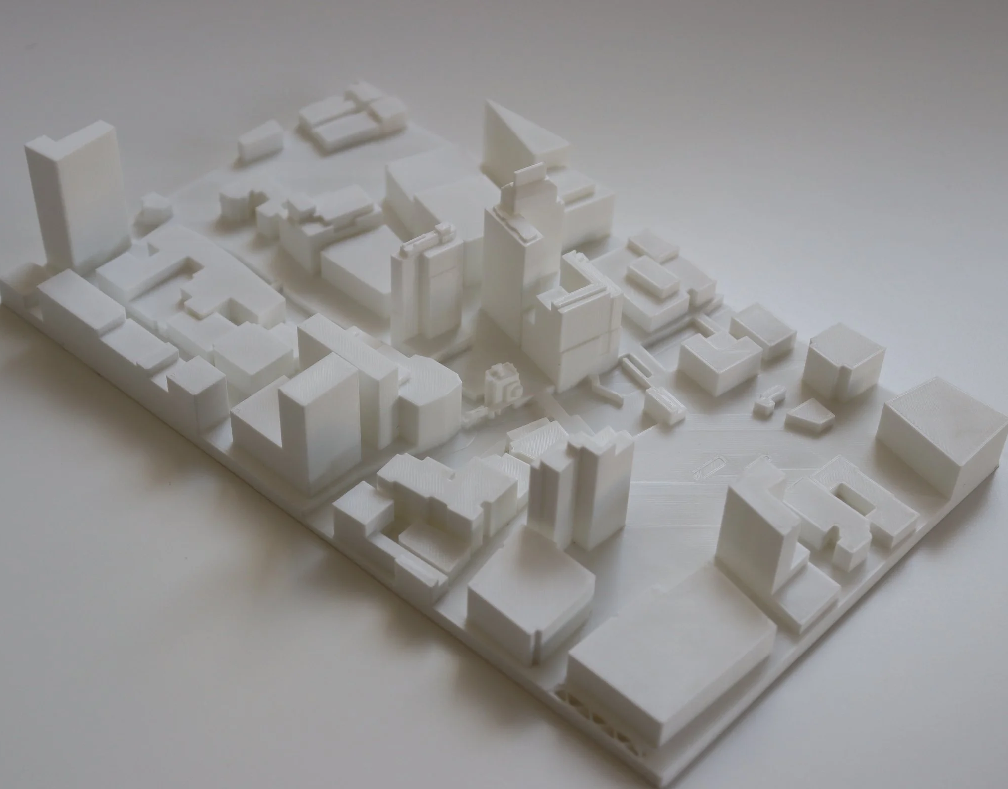 White architectural model of an urban development with various buildings and structures on a flat base.