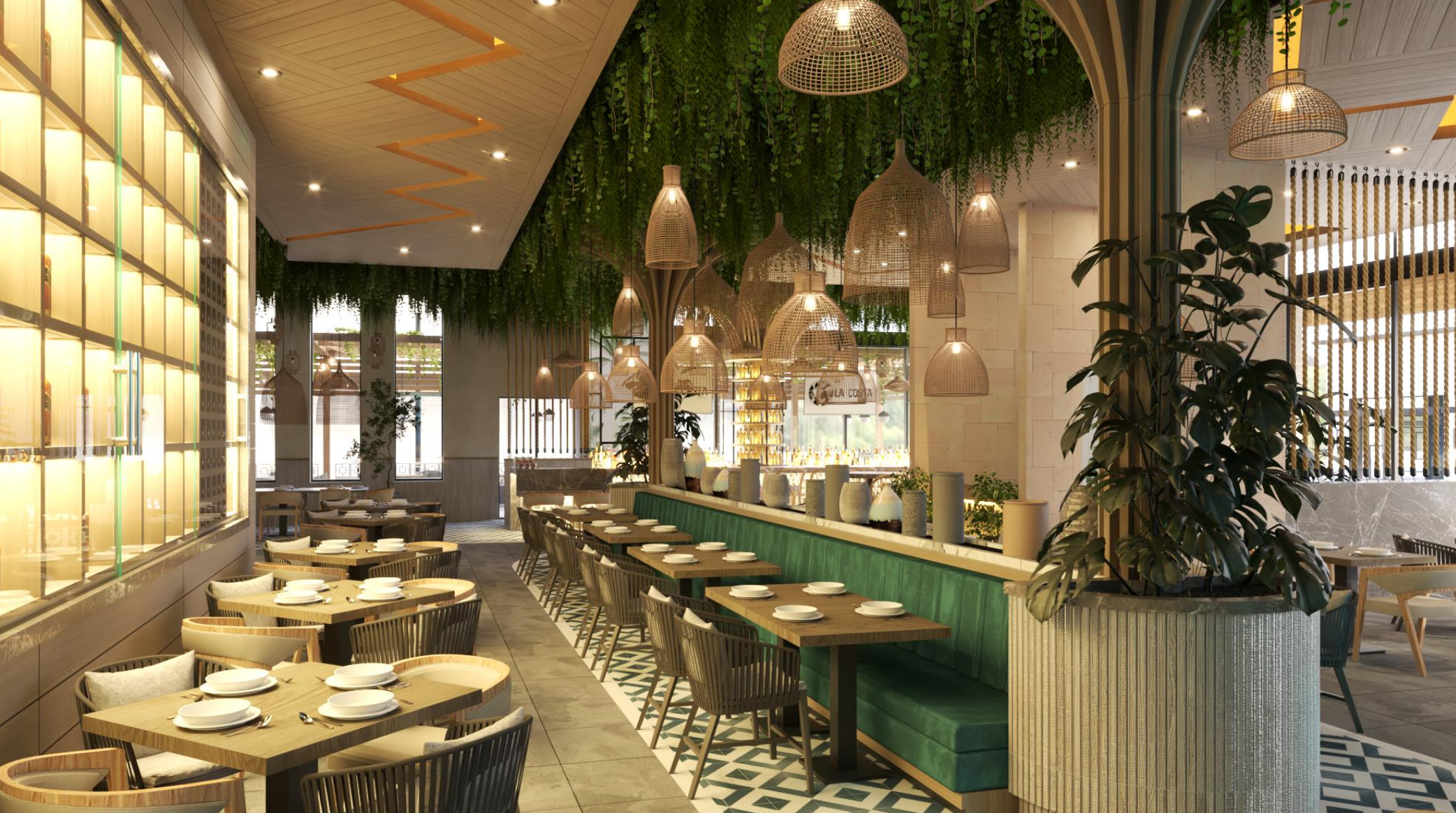 Modern restaurant interior with wooden tables, white plates, and chairs with pillows. A long green cushioned seating runs parallel to a bar with vases and hanging wicker light fixtures. Green plants and decorative elements are visible throughout.