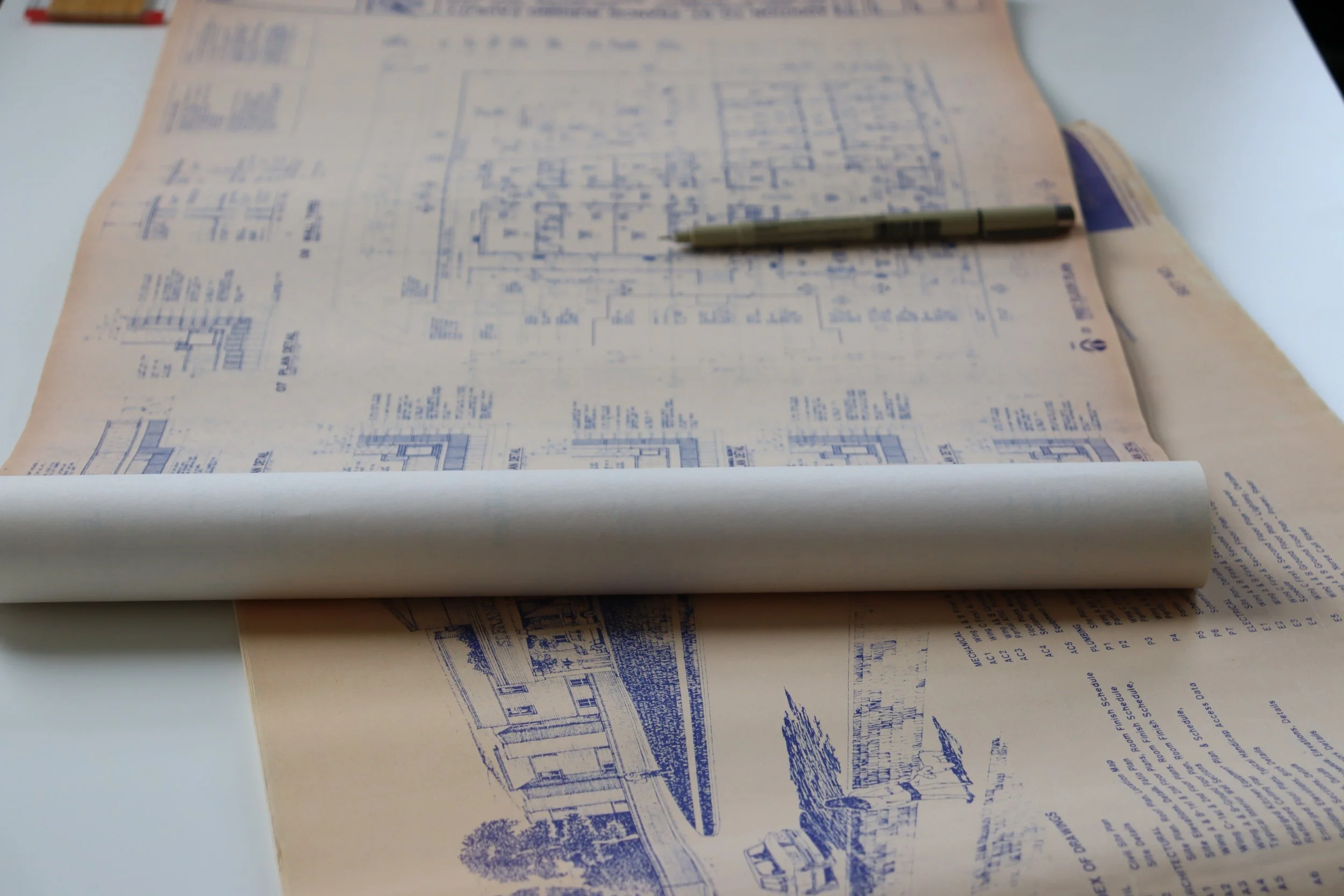 Architectural blueprint rolled out on a white table with a pen placed on top.