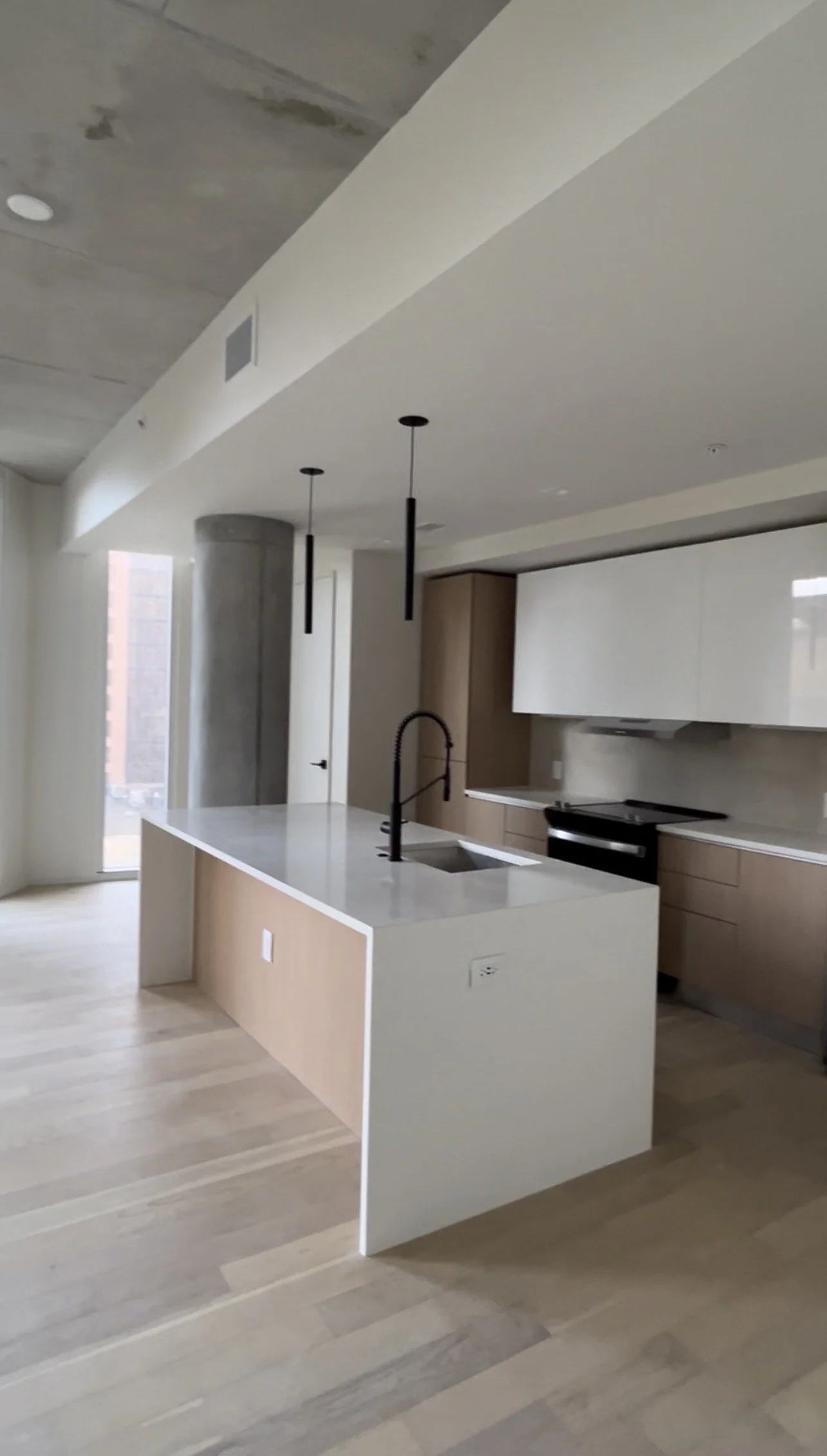 Modern kitchen with light wood flooring, a white island with a black faucet, hanging pendant lights, and white and wood cabinetry.