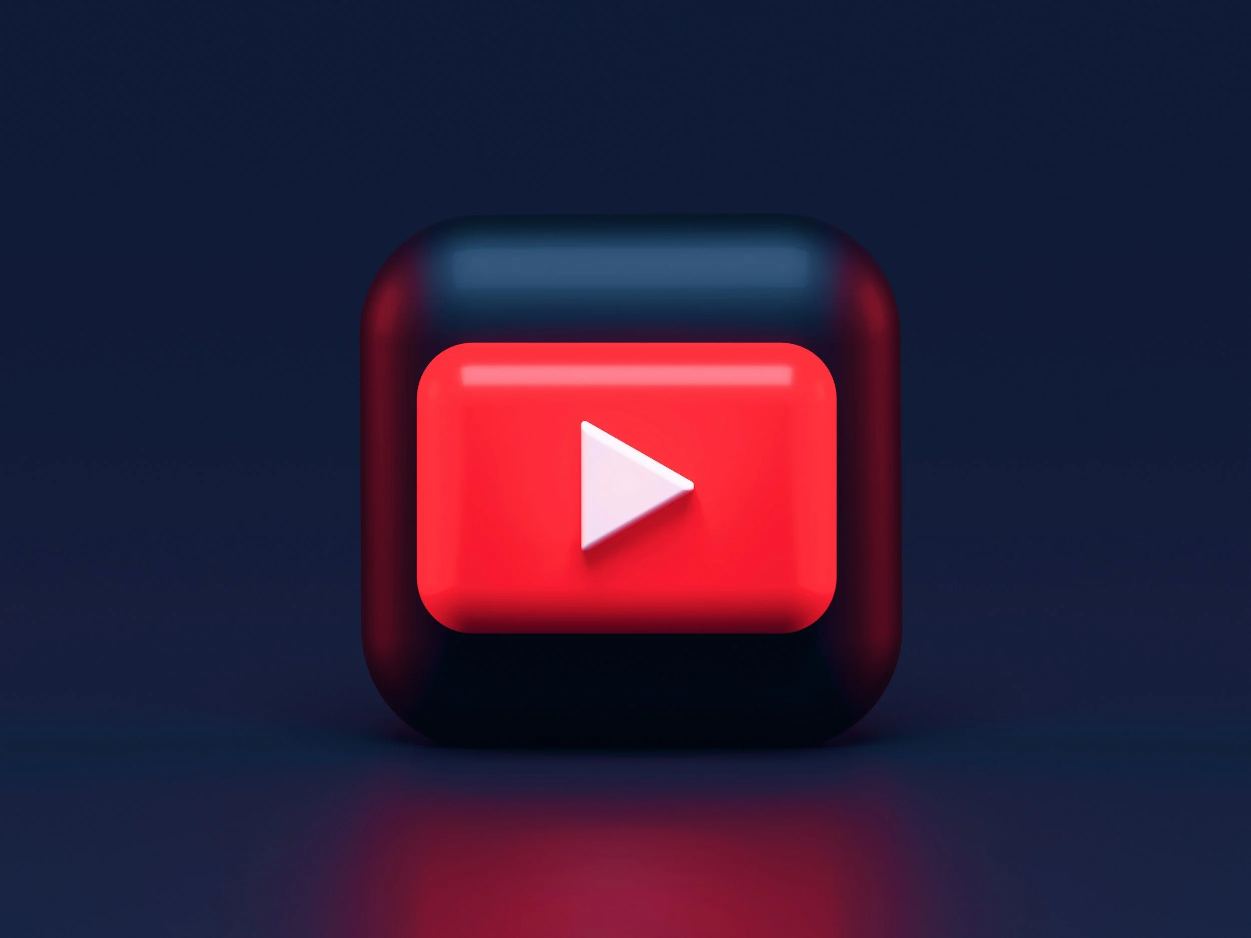 A 3D digital illustration of the YouTube app icon, featuring a red play button on a black square background with rounded edges, set against a dark background.