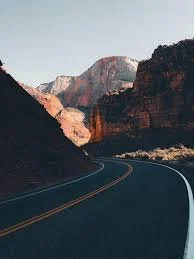 A winding road through the Grand Canyon with cliffs and a blue sky.