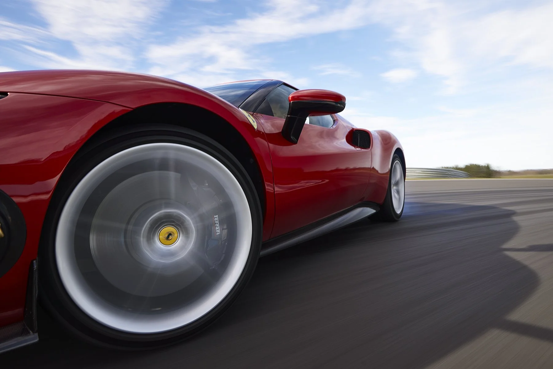 Voiture de course rouge sur une piste en mouvement rapide, ciel bleu avec quelques nuages.