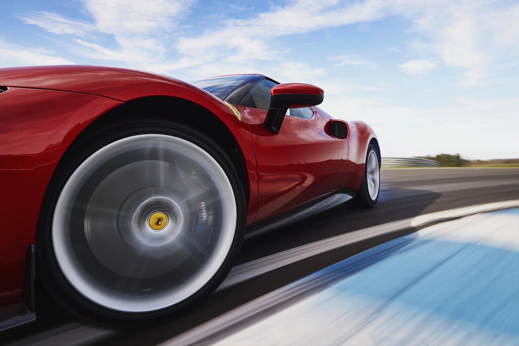 Une voiture de course Ferrari rouge en mouvement sur un circuit, vue en gros plan sur la roue et le côté de la voiture contre un ciel bleu.