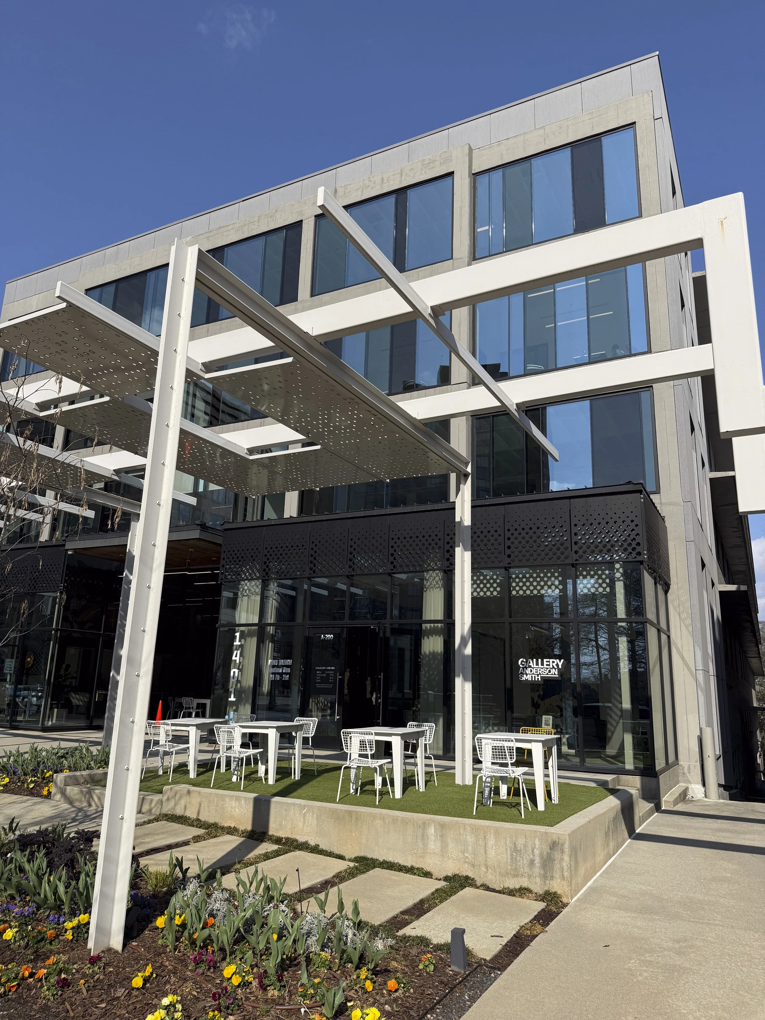 Modern multi-story building with large glass windows and an outdoor seating area with white tables and chairs.