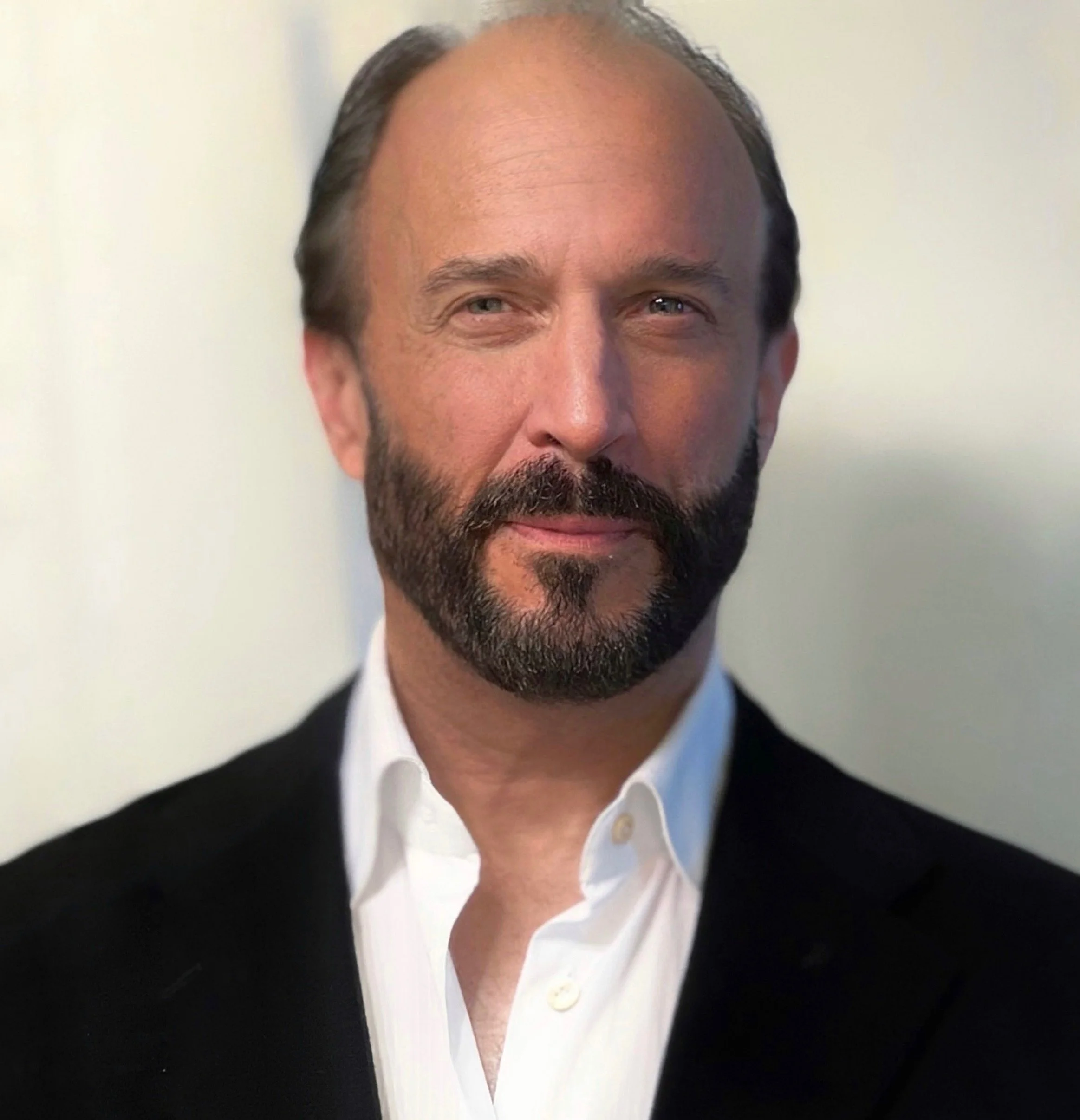Black and white portrait of a man with short hair, beard, and mustache, wearing a dark shirt, with a blurred indoor background.