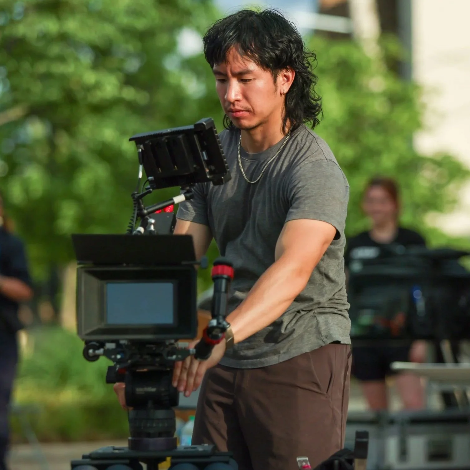 Director of Photography, Andy G Cat, operating a professional camera outdoors with green trees in the background, on the set of A Case For Coping.