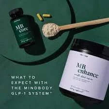 A bottle of MB Core supplement, a spoon with powder, and a container of MB Enhance supplement on a dark green surface.