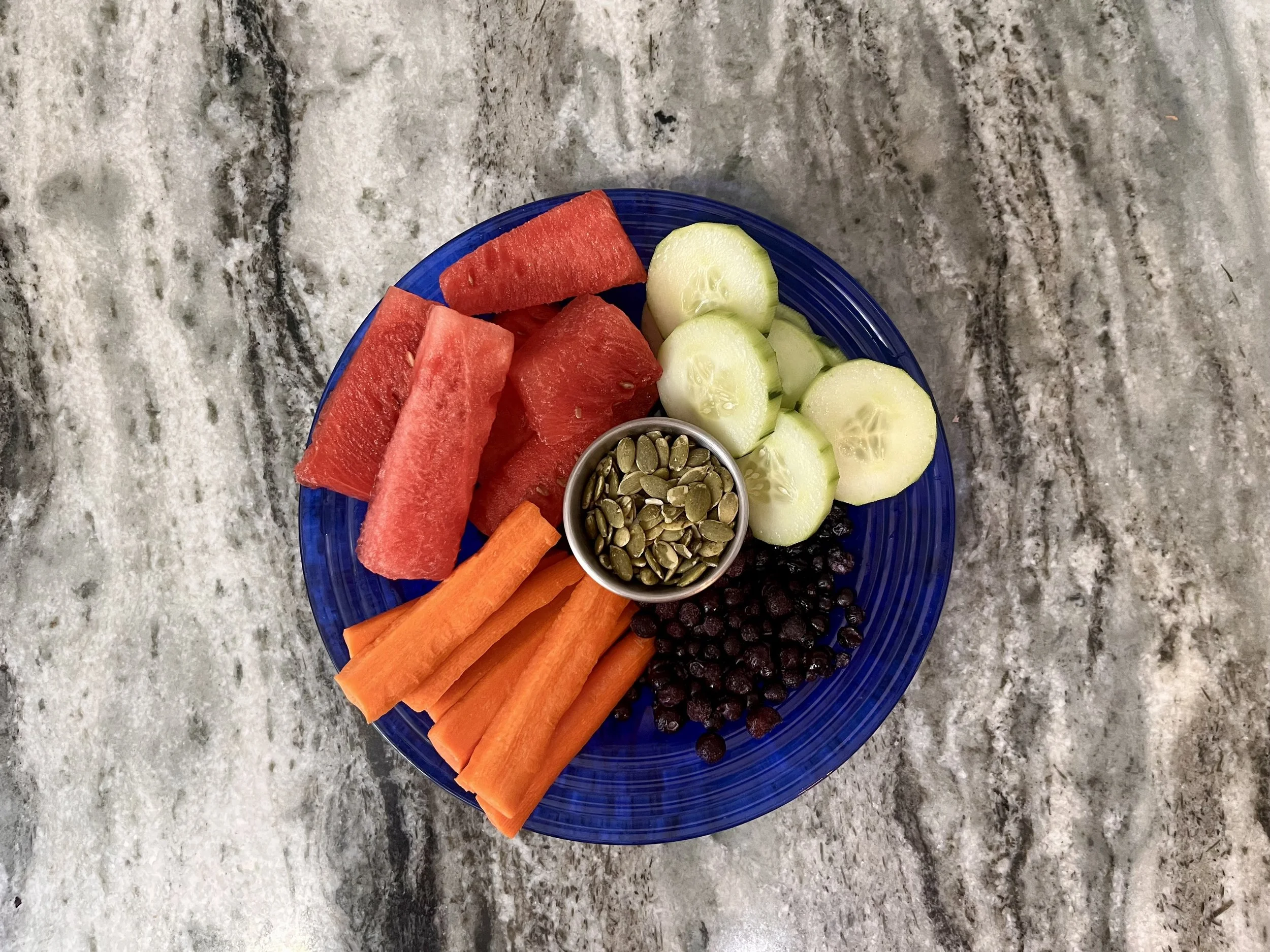 Assorted fresh foods including salmon, blueberries, strawberries, broccoli, tomatoes, spinach, pumpkin seeds, walnuts, oats, almonds, olive oil, and leafy greens on white plates and bowls.