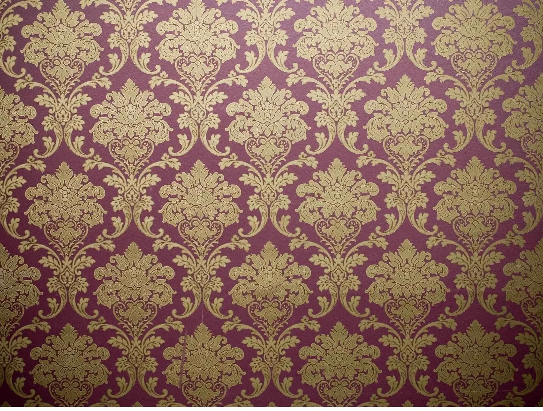 Gold ornate floral pattern on a purple background, resembling damask wallpaper.