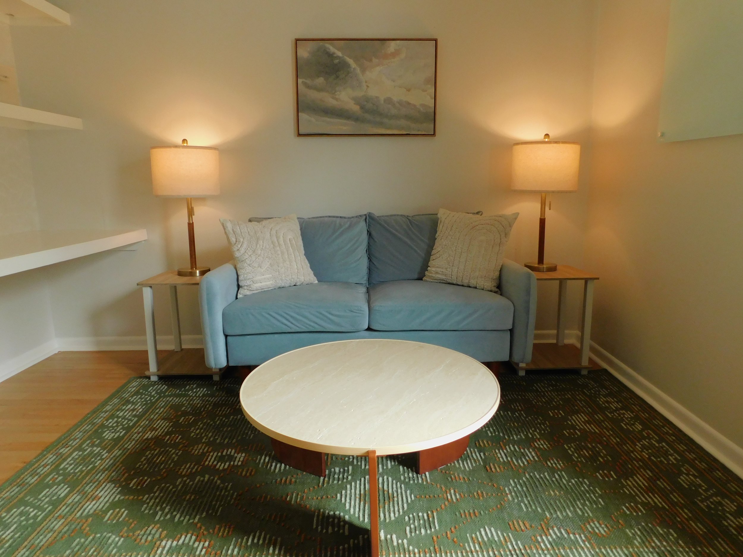 Suite B therapy setup with light blue couch, balanced lamp lighting, modern artwork, and warm sensory-aware design.