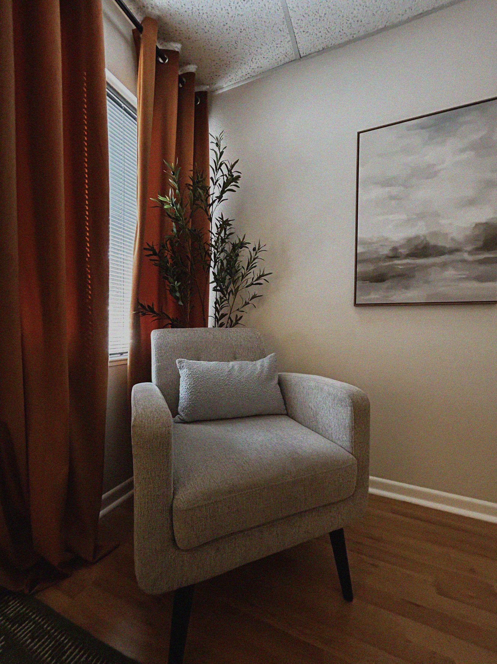 Suite B at Luzia Therapy Suites featuring a therapist chair, blue accent pillow, natural light, and modern artwork in a calming healing environment.