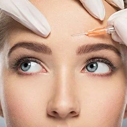 A woman receiving Botox injection in her forehead from a healthcare professional wearing gloves.