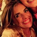 Two women smiling closely together, one with long blonde hair and the other with long dark hair.