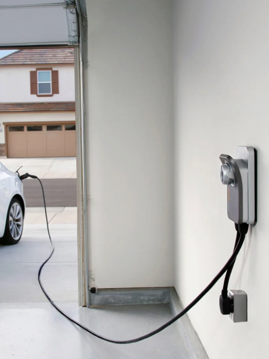 Electrical charging station in a garage with a charging cable connected to a car outside.