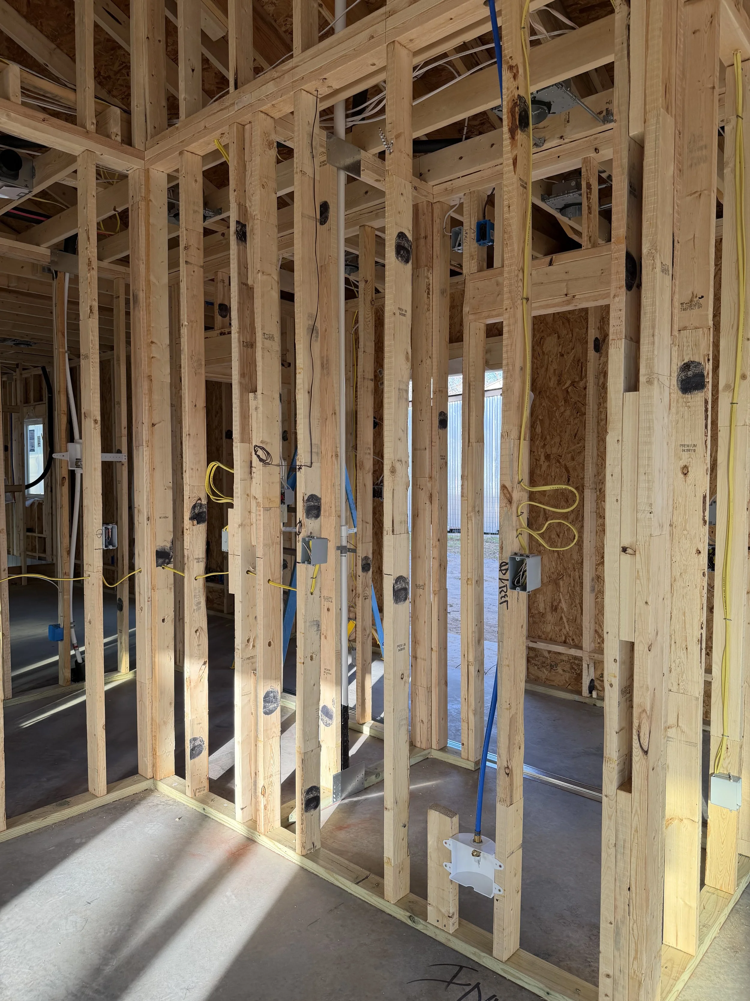 Interior view of a house under construction, showing wood framing, electrical wiring, and outlets.