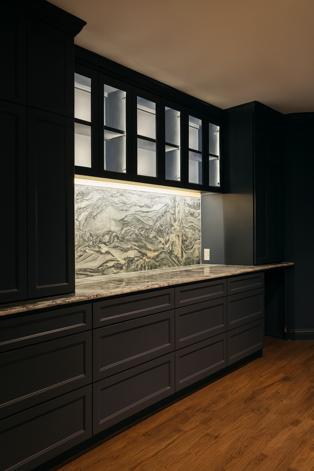 Kitchen with dark cabinetry, marble countertop, and marble backsplash, featuring glass-front upper cabinets and wooden flooring.