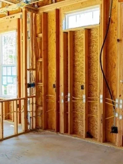 Unfinished interior of a room under construction with exposed wooden studs, electrical wiring, and a window showing an outdoor view.