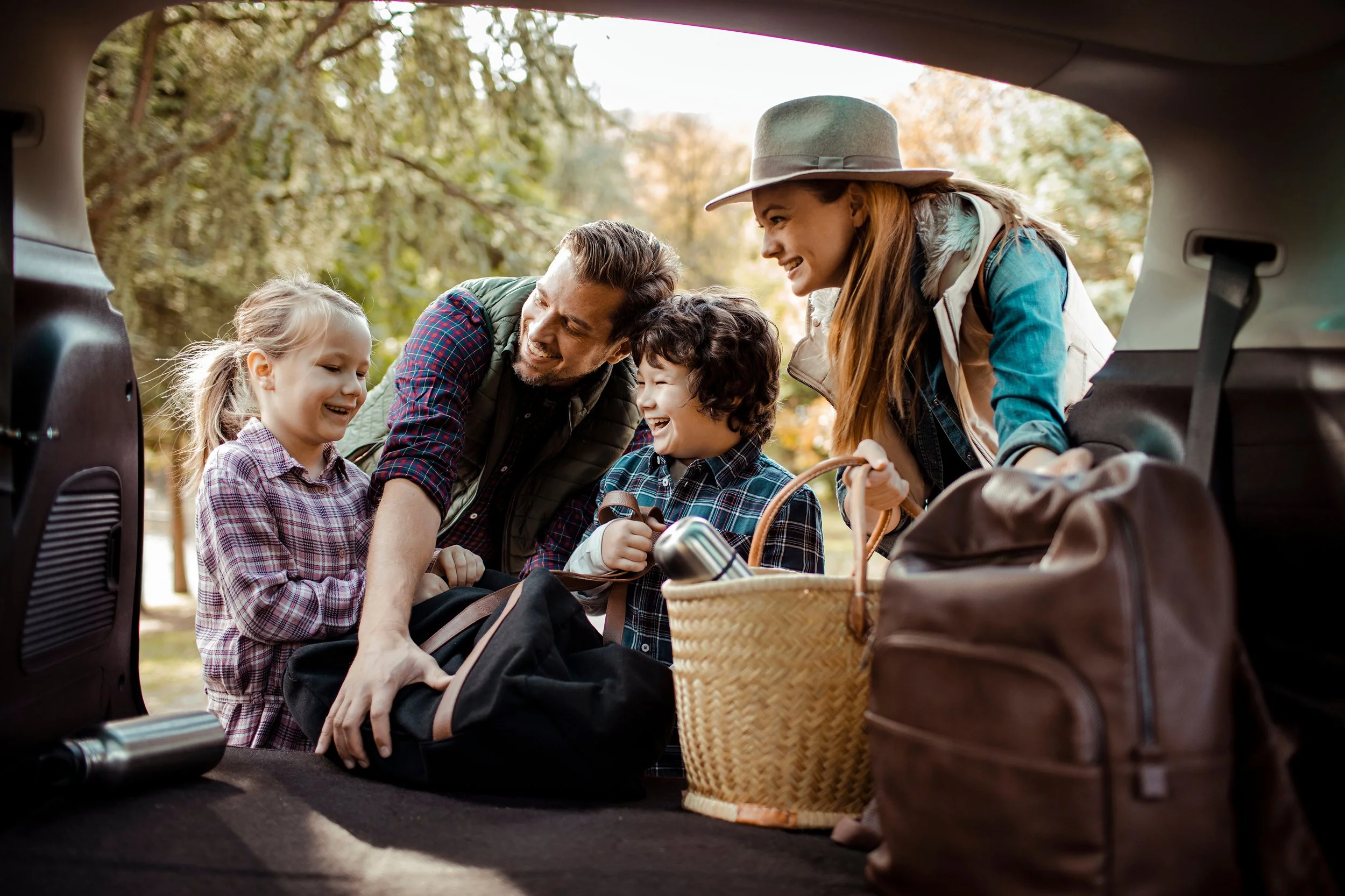 Family packing items into car trunk outdoors on a sunny day.