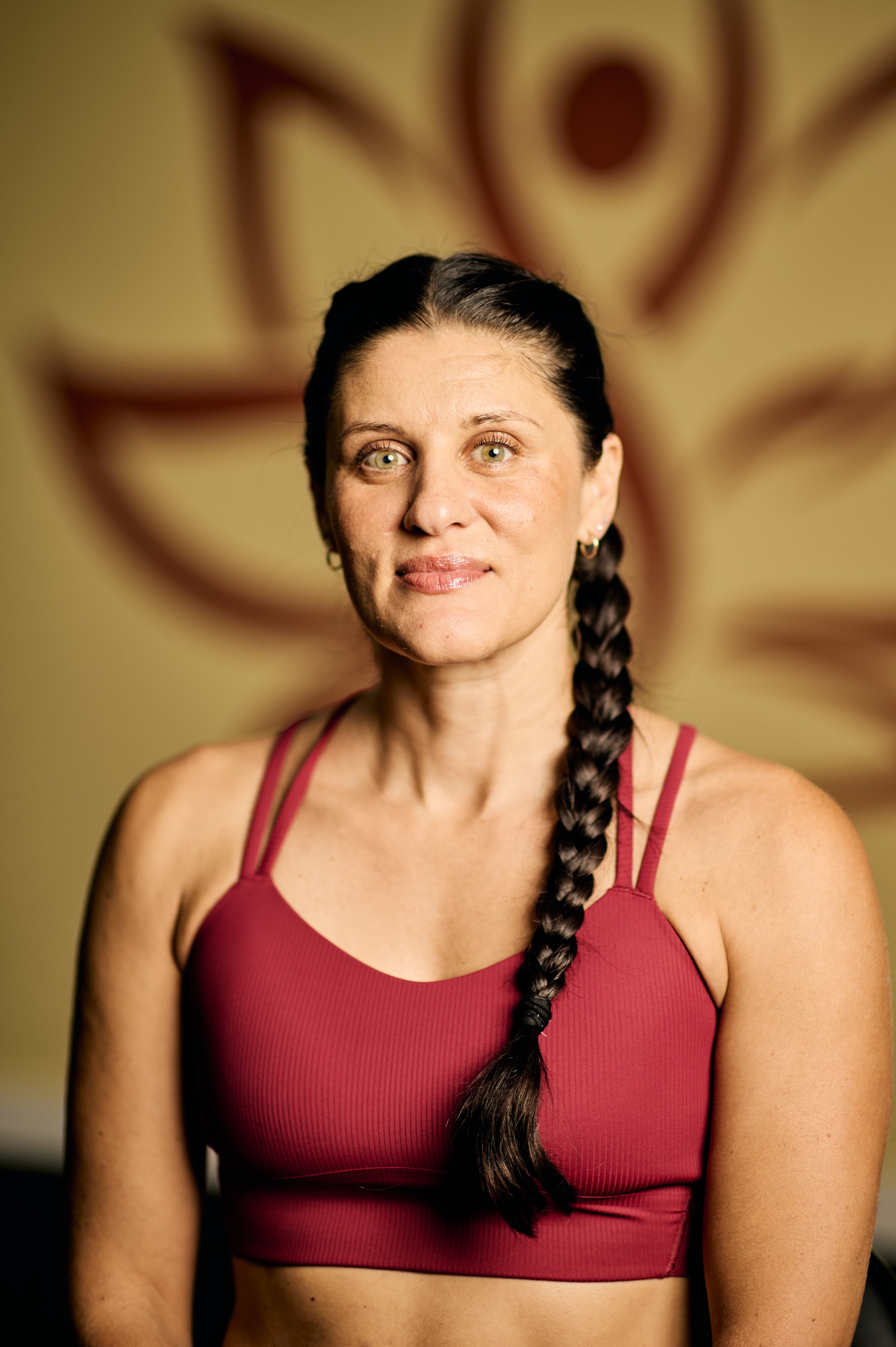 A woman with dark hair in a braid, wearing a red sports bra, standing in front of a colorful abstract background.