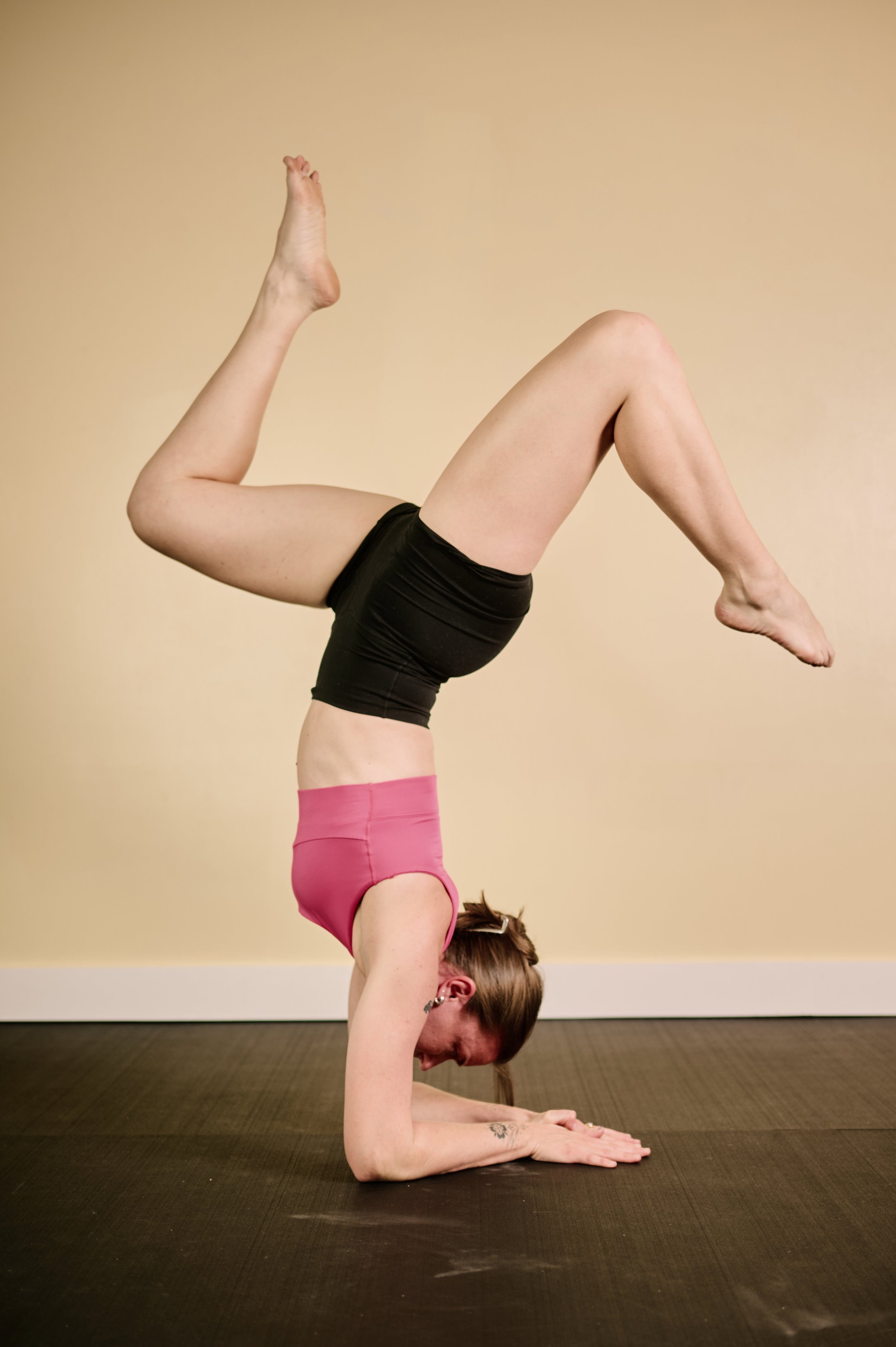 A woman doing a headstand yoga pose indoors on a black mat.