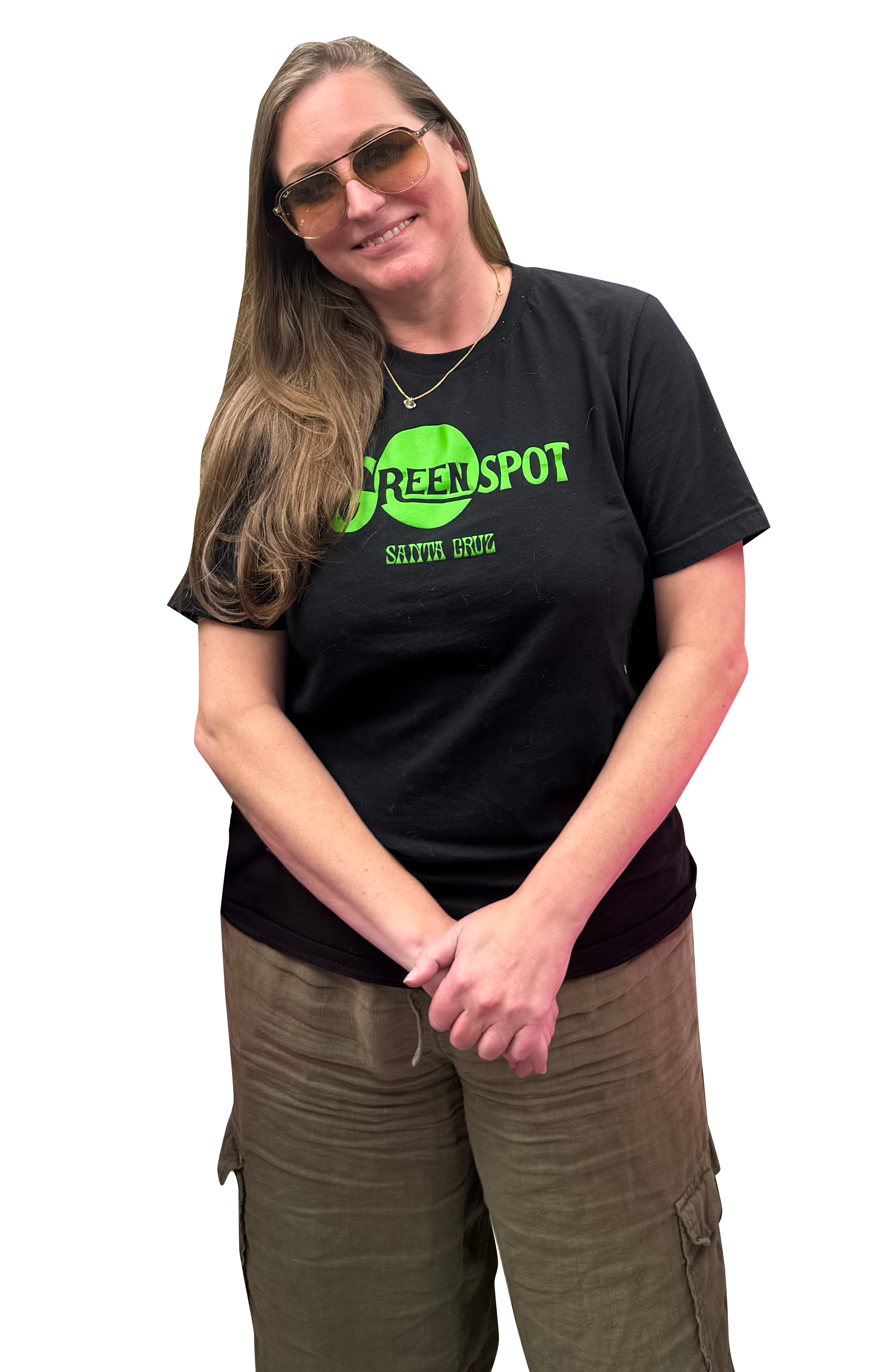 A woman wearing sunglasses and a black T-shirt that reads 'GREENSPOT SANTA CRUZ,' smiling with her hands clasped in front of her, standing against a plain background.