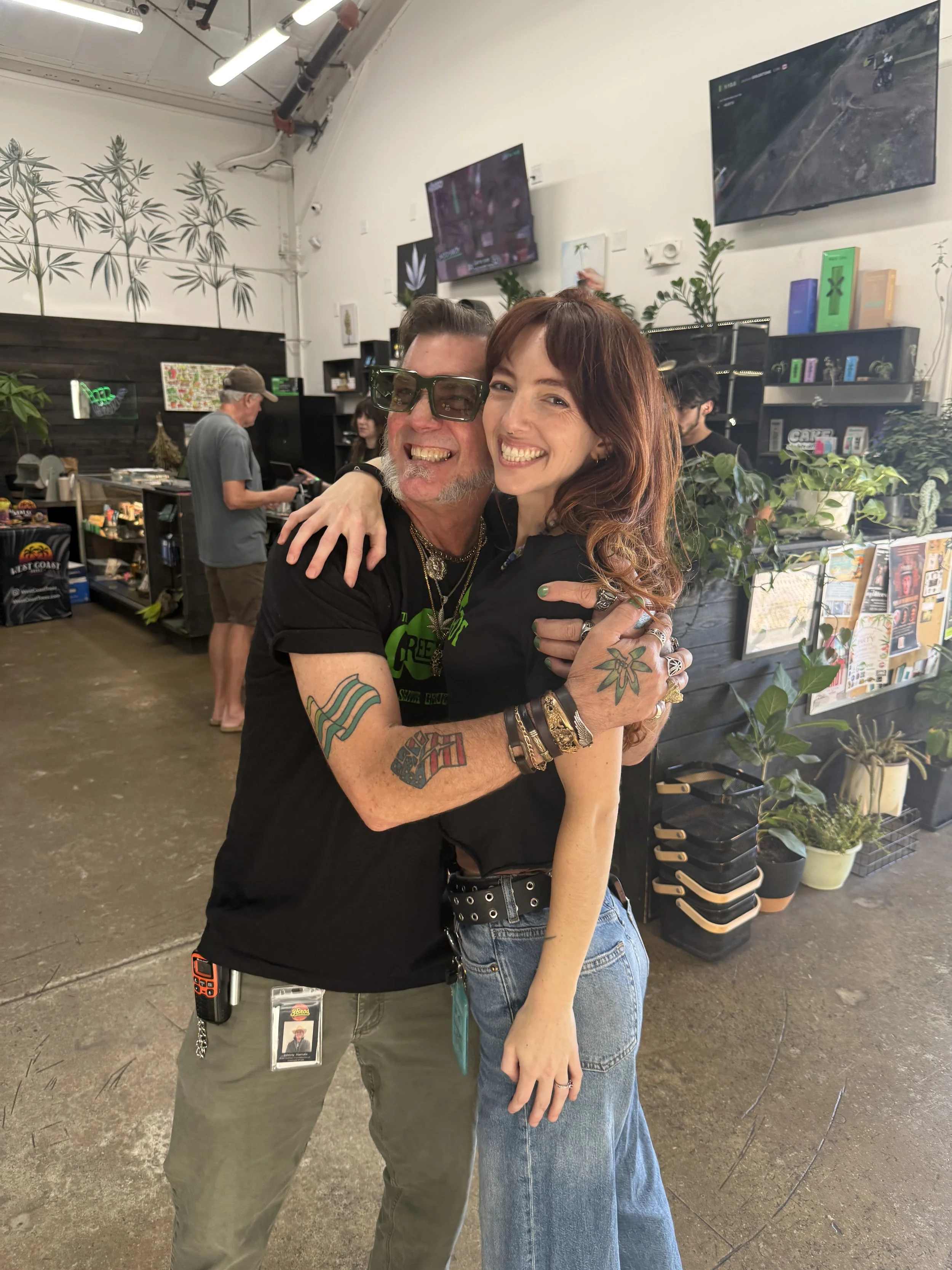 Two people embracing and smiling in a store with plants and televisions in the background.