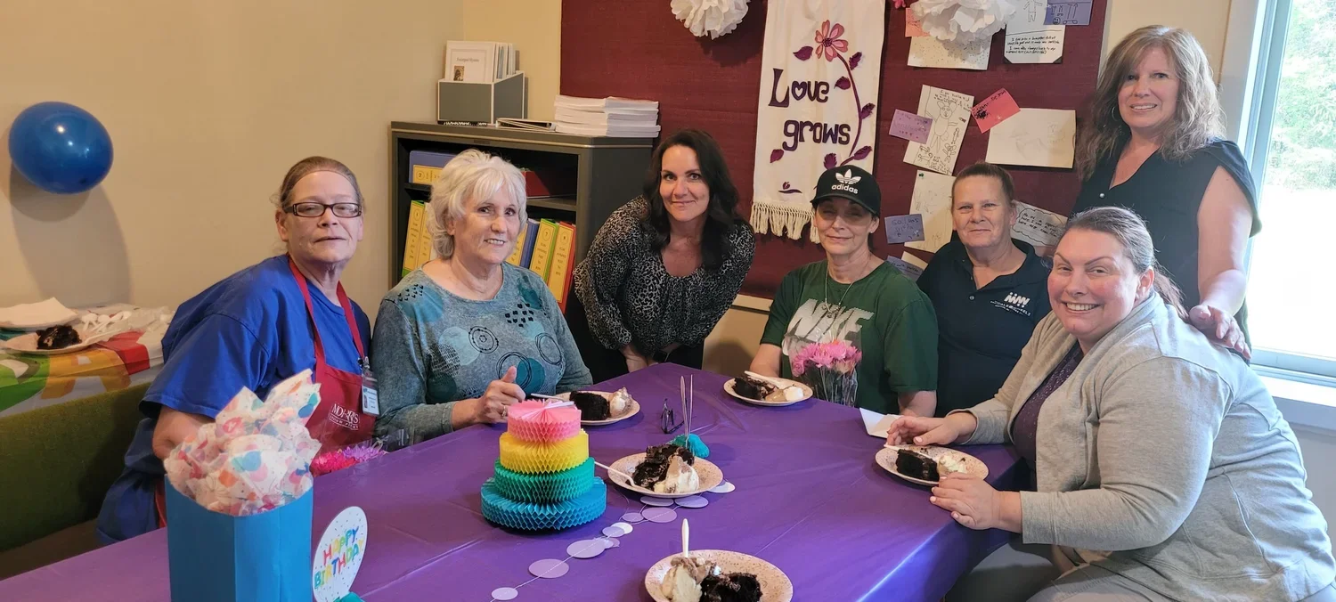 Group of women celebrating birthday with cake, gifts, and decorations.